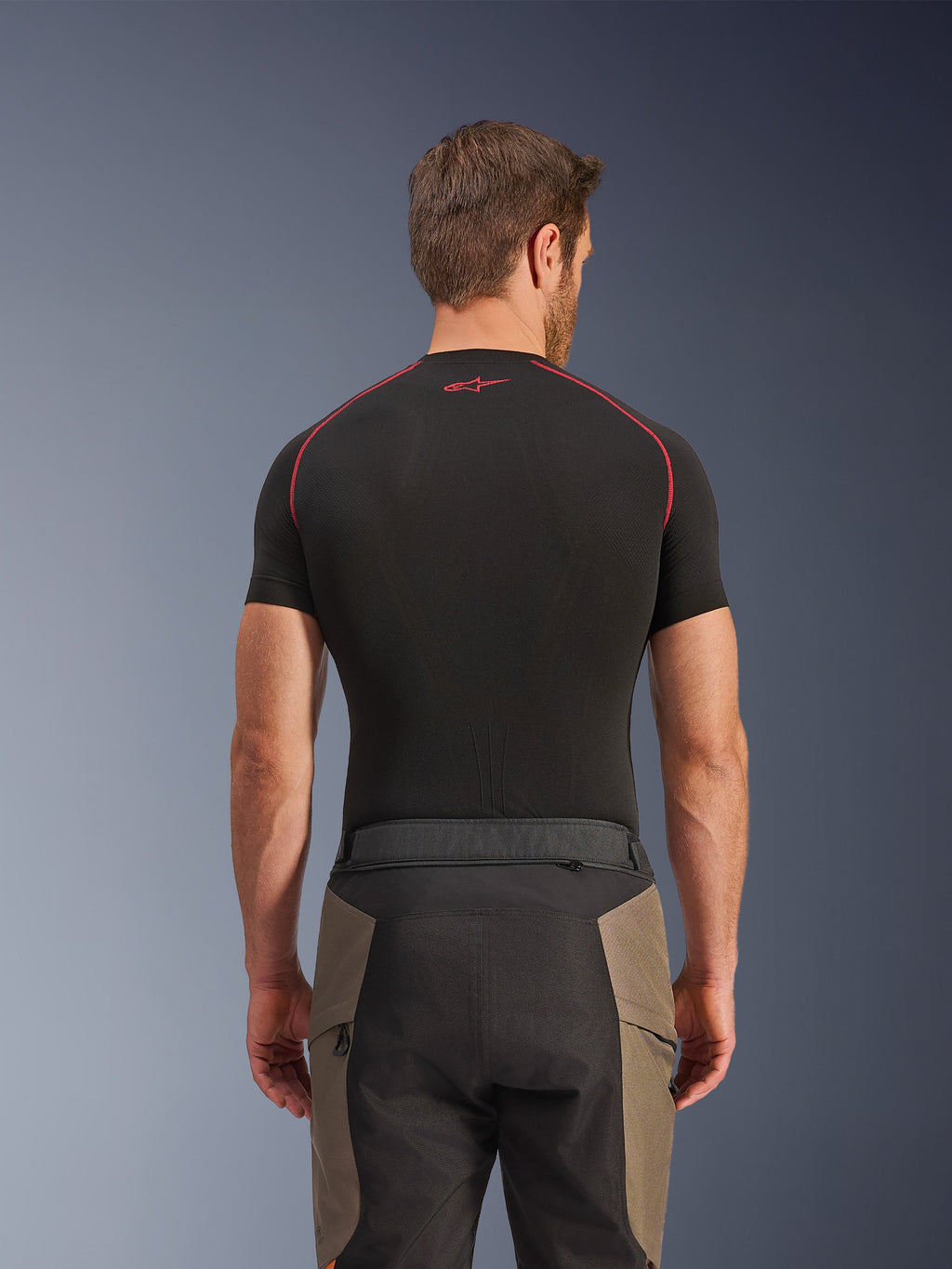 Alpinestars Cusco Drystar® Hose, Adventure-Motorradhose, Walnut Black, Rückansicht mit Taillendetails und Color-Blocking-Design, getragen mit einem schwarzen kurzärmeligen Base-Layer mit roten Nähten und Logo