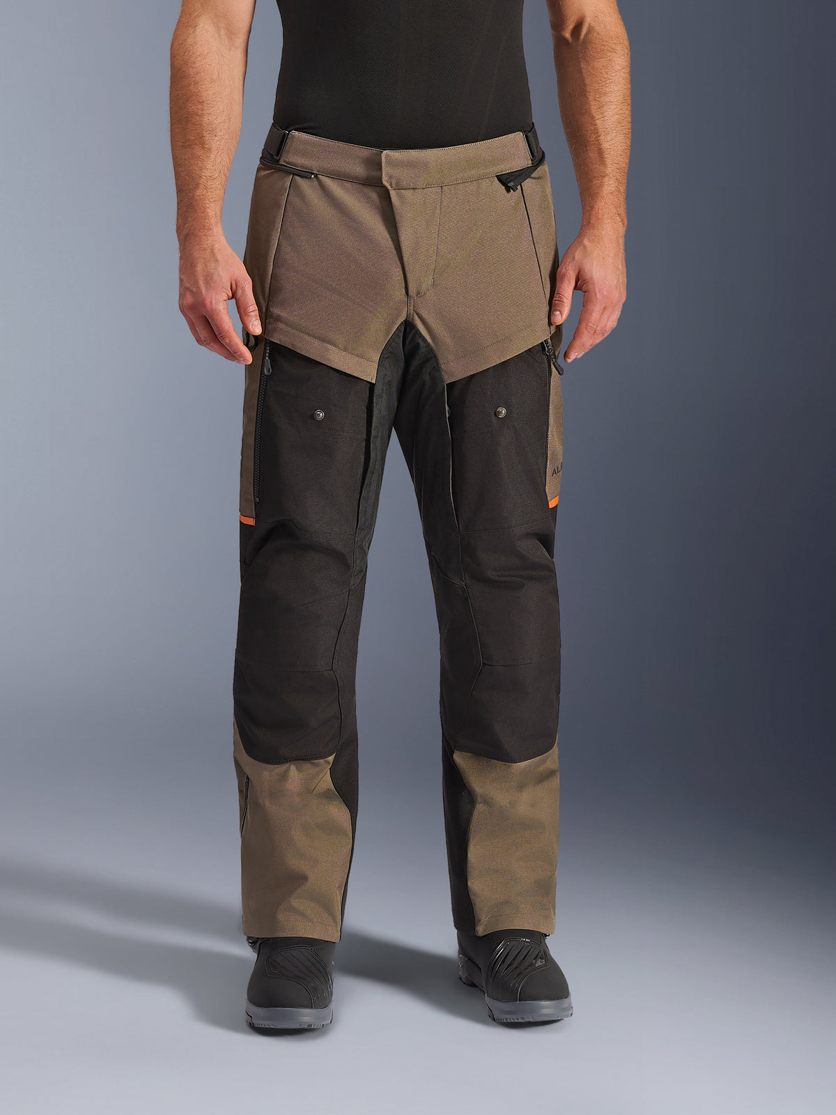 Alpinestars Cusco Drystar® Hose, Adventure-Touring-Motorradhose, Walnussbraun und Schwarz mit orangefarbenen Akzenten, Vorderansicht am Modell, technische Textilkonstruktion, Cargotaschen und Belüftungsreißverschlüsse, getragen mit schwarzen Motorradstiefeln