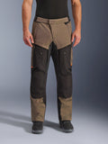 Alpinestars Cusco Drystar® Hose, Adventure-Touring-Motorradhose, Walnussbraun und Schwarz mit orangefarbenen Akzenten, Vorderansicht am Modell, technische Textilkonstruktion, Cargotaschen und Belüftungsreißverschlüsse, getragen mit schwarzen Motorradstiefeln