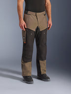 Alpinestars Cusco Drystar® Hose, Adventure-Motorradhose, Walnut Black, abgebildet an einem Modell mit schwarzen Stiefeln, in einem braun-schwarzen Multi-Panel-Design mit Reißverschlusstaschen und verstärkten Knien für Touren