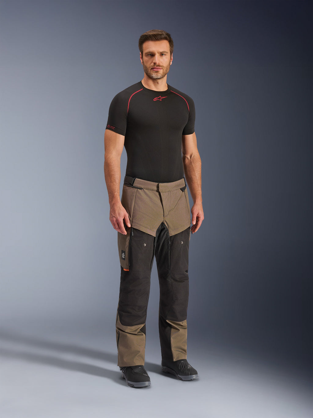 Alpinestars Cusco Drystar® Hose, Adventure-Motorradhose, Walnuss und Schwarz, getragen von einem Modell mit schwarzem Base-Layer und Stiefeln, mit großen Cargo-Taschen am Oberschenkel, Belüftungsreißverschlüssen und einem robusten, zweifarbigen Design.