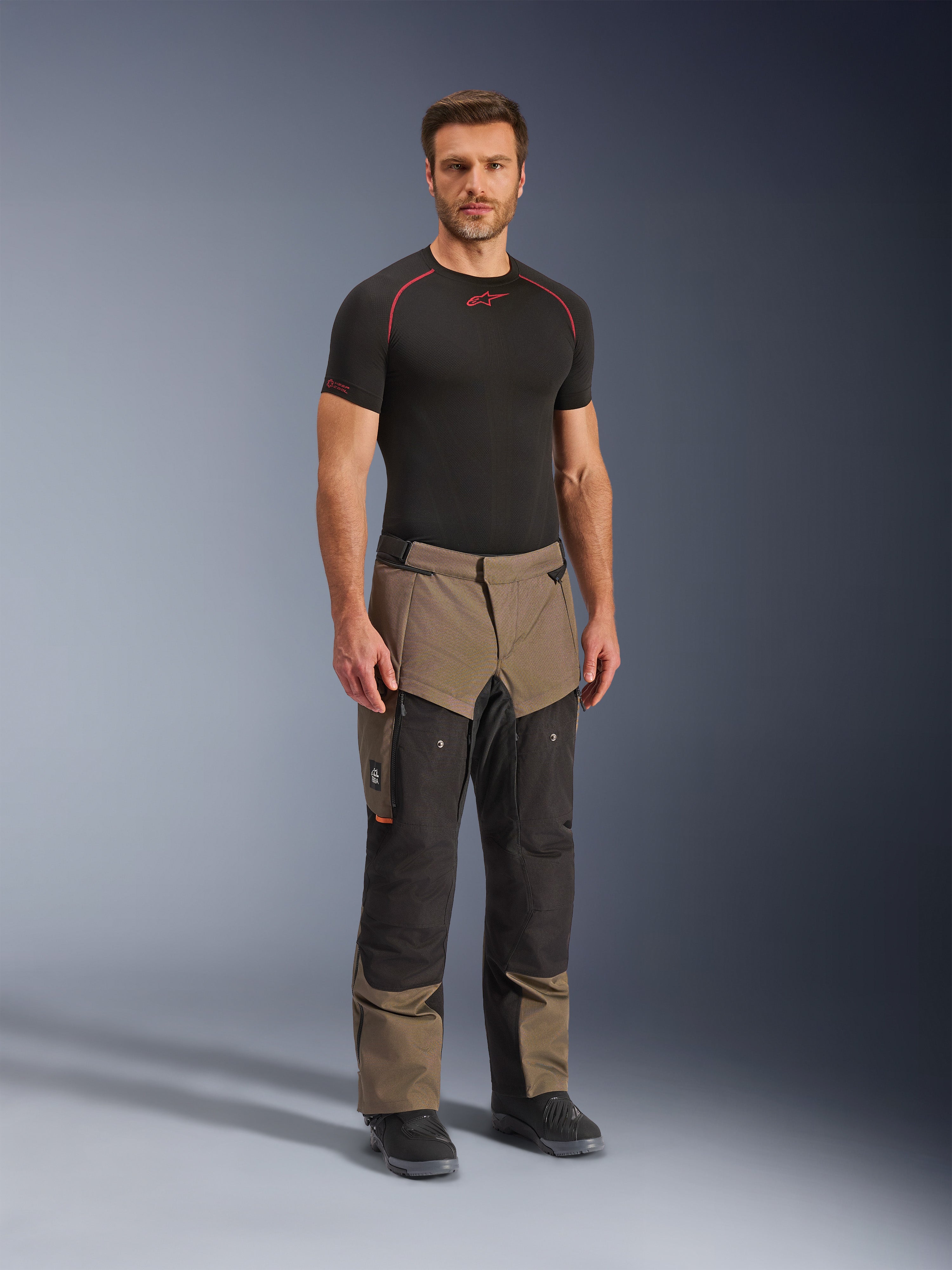Alpinestars Cusco Drystar® Hose, Adventure-Motorradhose, Walnuss und Schwarz, getragen von einem Modell mit schwarzem Base-Layer und Stiefeln, mit großen Cargo-Taschen am Oberschenkel, Belüftungsreißverschlüssen und einem robusten, zweifarbigen Design.
