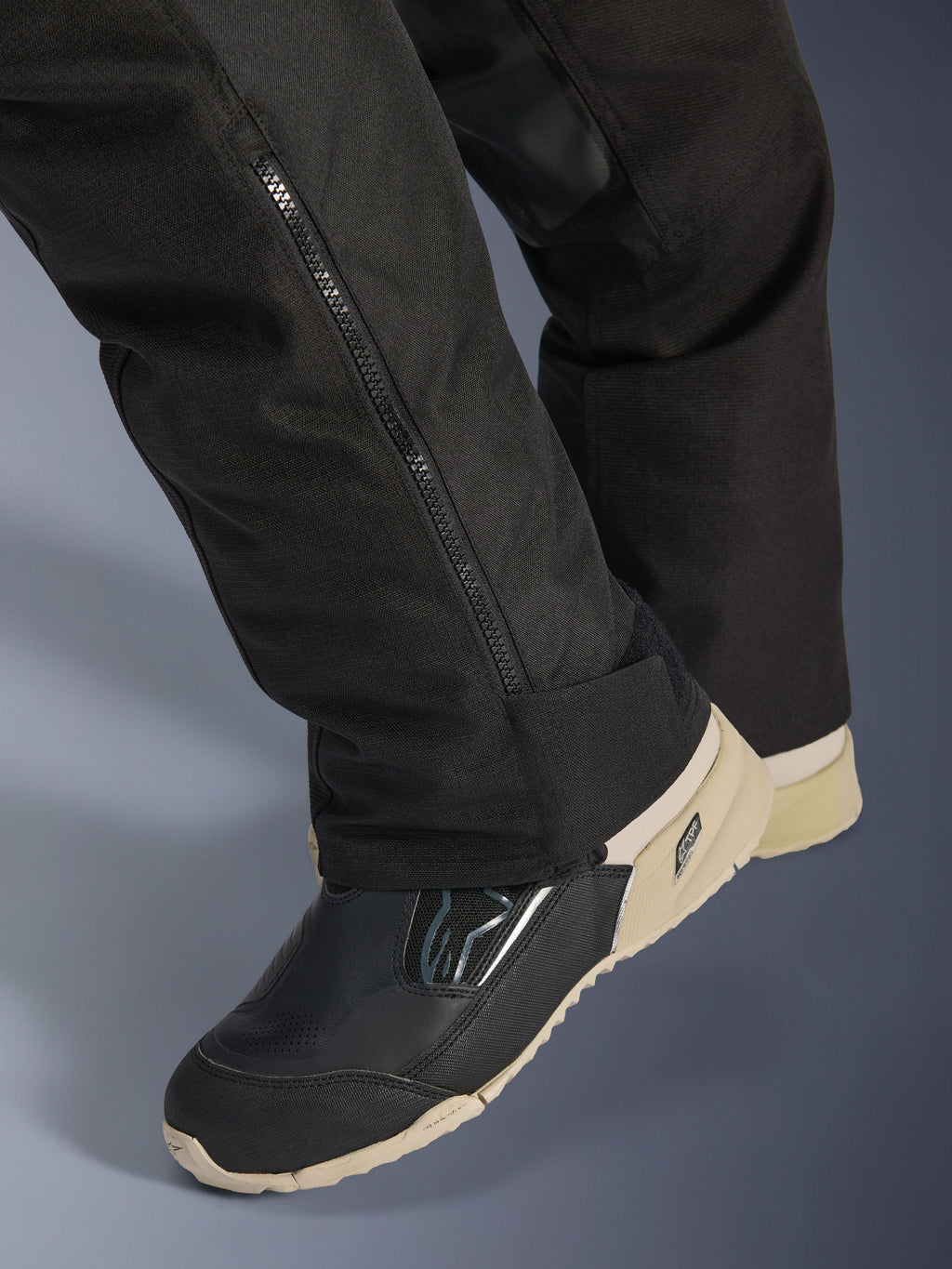 Alpinestars Stella Andes V4 Drystar® Hose, Schwarz, Nahaufnahme des unteren Hosenbeins mit seitlichem Reißverschluss zur Stiefelanpassung, strapazierfähiges Textilmaterial, getragen mit schwarz-beigen Motorradstiefeln, abenteuertaugliches funktionales Design