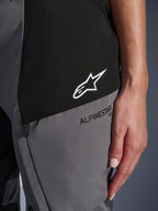 Alpinestars Stella Andes V4 Drystar® Damen-Hose, Nahaufnahme in Schwarz und Dunkelgrau, weißes Stern-Logo auf schwarzem Panel, schwarzes Alpinestars-Branding auf grauem Panel, technisches Textilgewebe und Detail der Reißverschlusstasche.