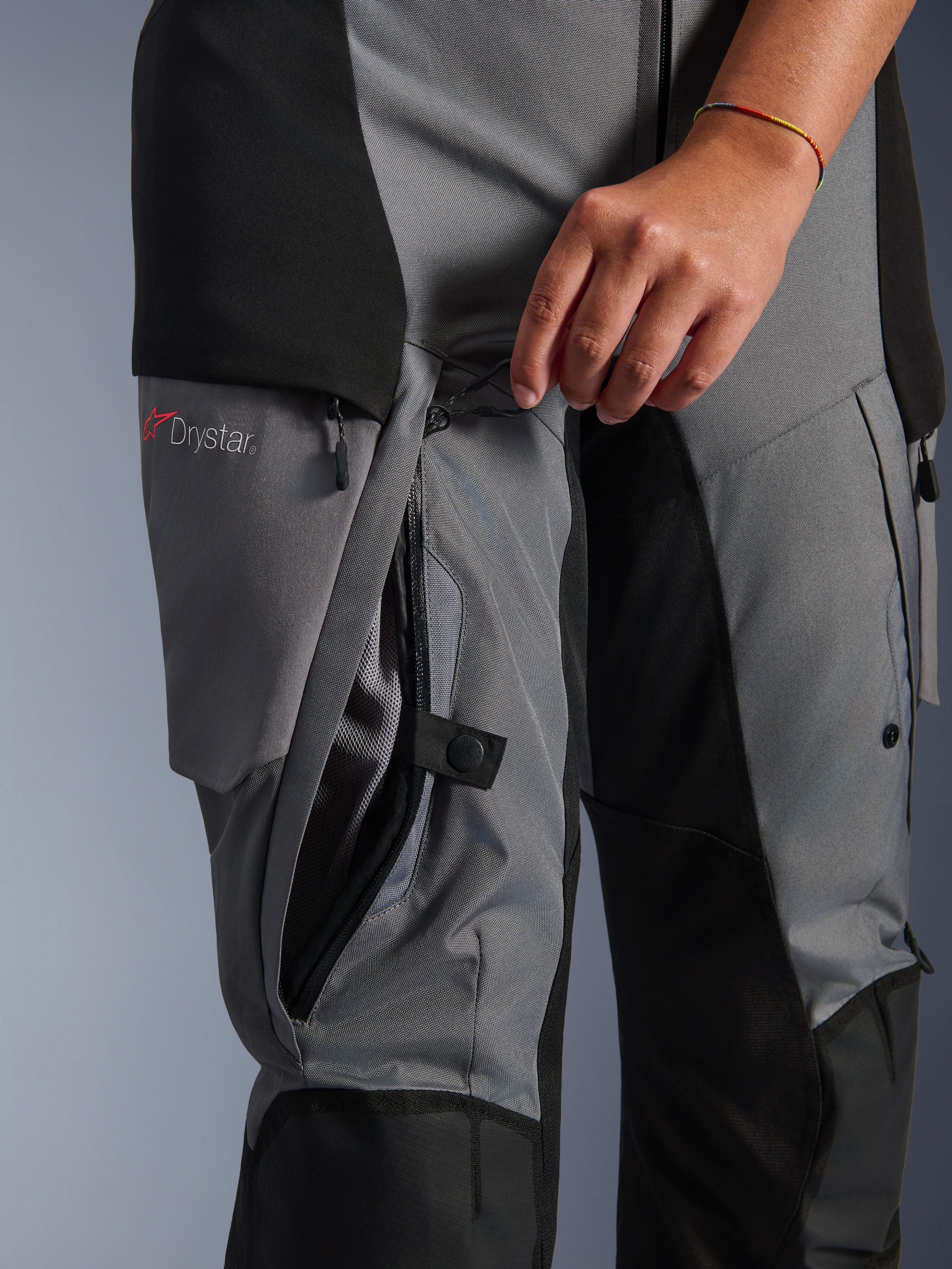 Alpinestars Stella Andes V4 Drystar Hose, Textil in Schwarz und Dunkelgrau, Nahaufnahme der Oberschenkelbelüftung, die von Hand geöffnet wird, sichtbares Netzfutter, mit Drystar-Logo, Adventure-Motorradbekleidung