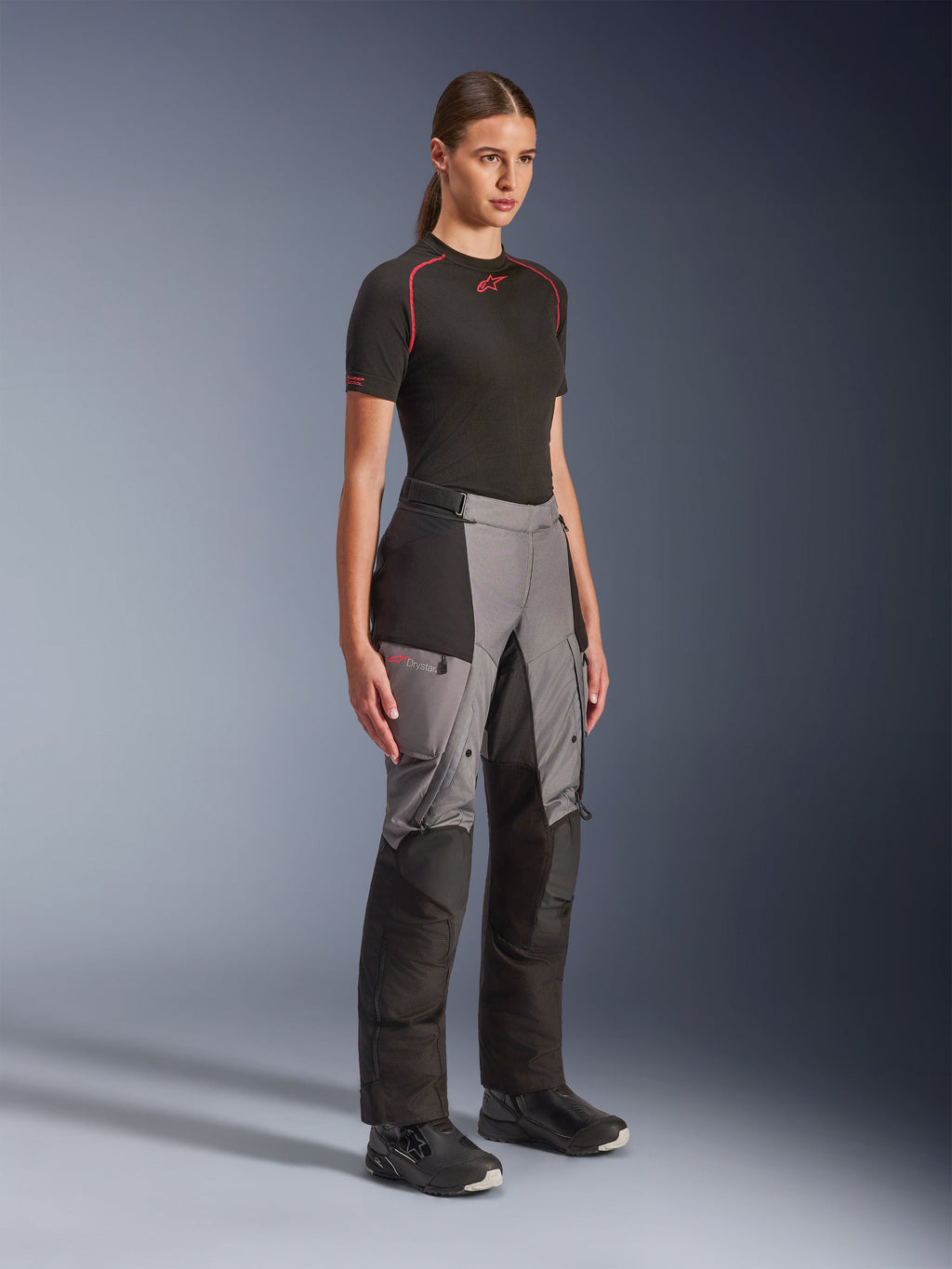 Alpinestars Stella Andes V4 Drystar® Hose, Adventure-Motorradhose für Damen, Schwarz und Dunkelgrau, getragen von einem Model mit schwarzem Alpinestars Base Layer und schwarzen Stiefeln, mit verstärkten Paneelen, rotem Drystar-Logo und Cargotaschen.