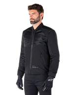 Alpinestars Mootant Waterproof Parka, modular black motorcycle jacket shown in its bomber configuration with mesh upper body panels and a ribbed collar, worn by a model with black riding gloves and pants, urban contemporary streetwear style.