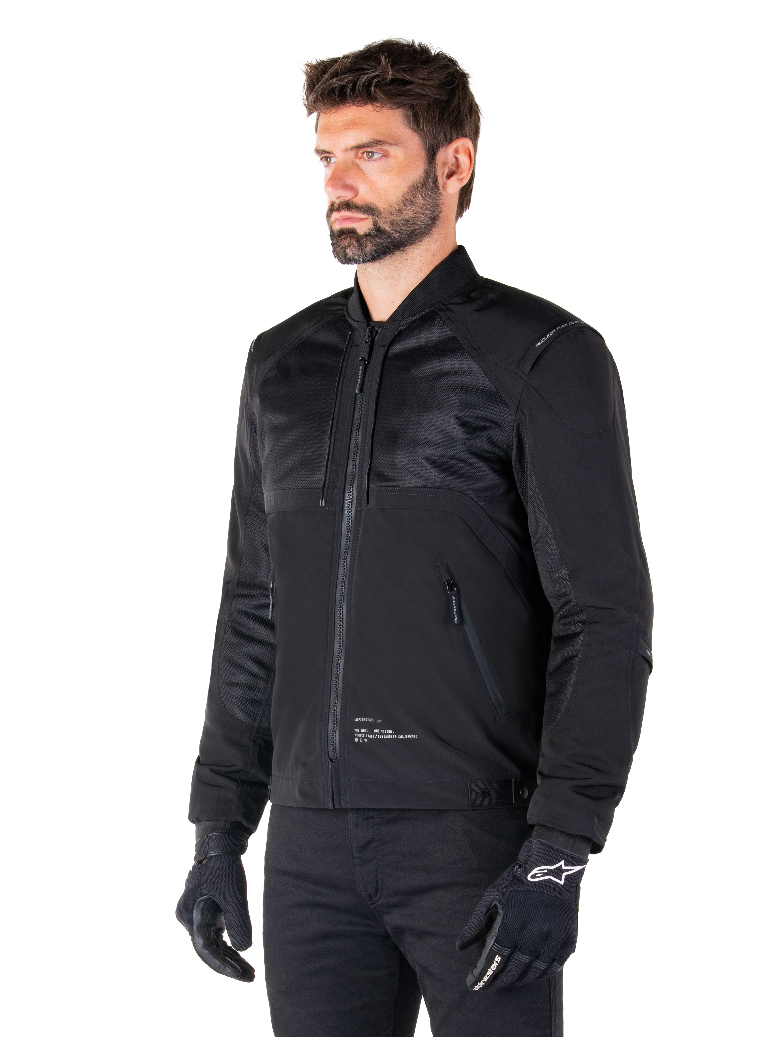 Alpinestars Mootant Waterproof Parka, modular black motorcycle jacket shown in its bomber configuration with mesh upper body panels and a ribbed collar, worn by a model with black riding gloves and pants, urban contemporary streetwear style.