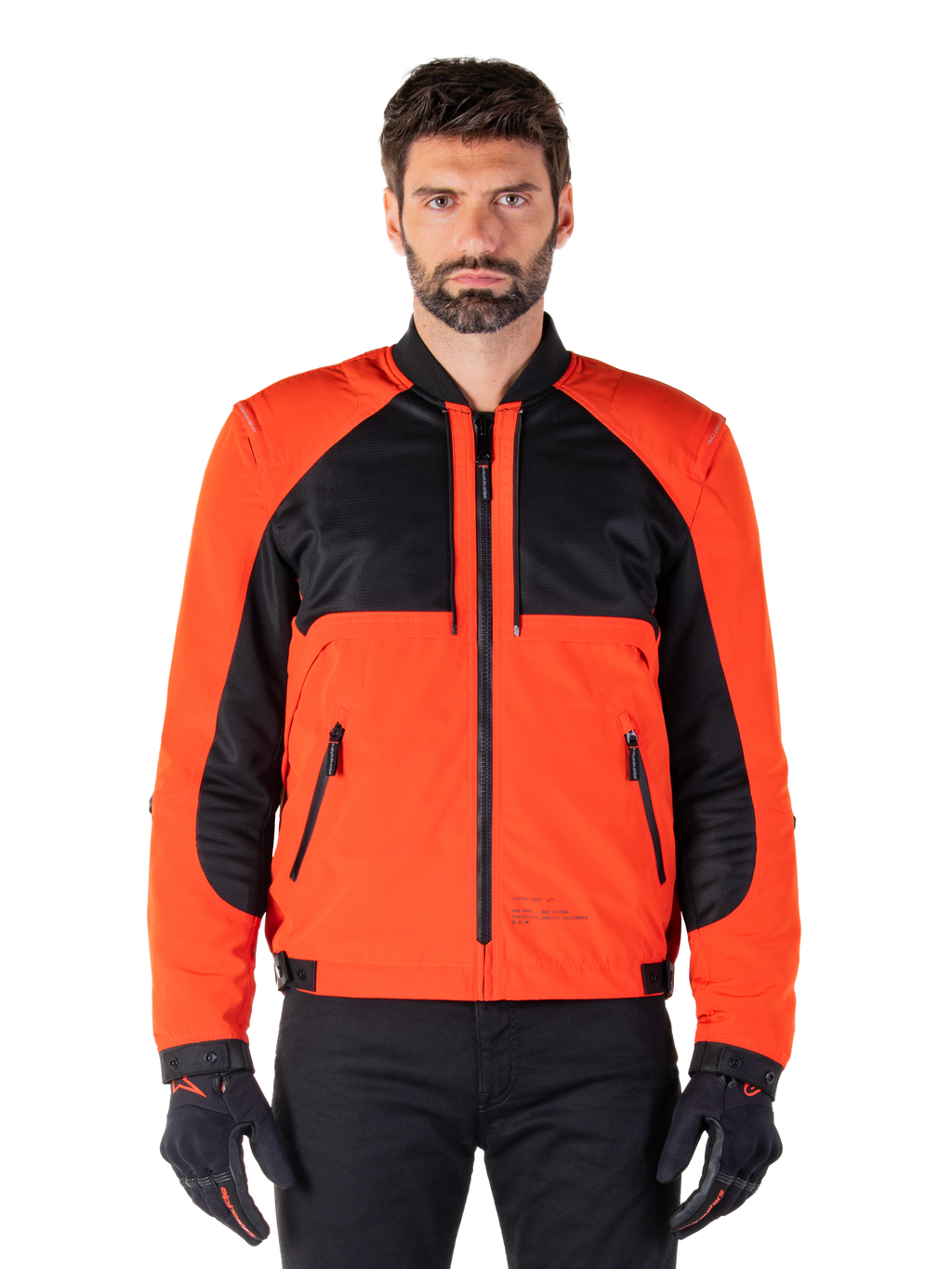 Alpinestars Mootant Wasserdichter Parka in Spicy Orange und Schwarz, modulare Motorradjacke in Bomberjacken-Konfiguration an einem männlichen Modell, mit schwarzen Mesh-Einsätzen im oberen Brustbereich, leuchtend orangefarbenem Torso und Ärmeln, Frontreißverschluss und Rippkragen, kombiniert mit schwarzen Handschuhen und einer schwarzen Hose.