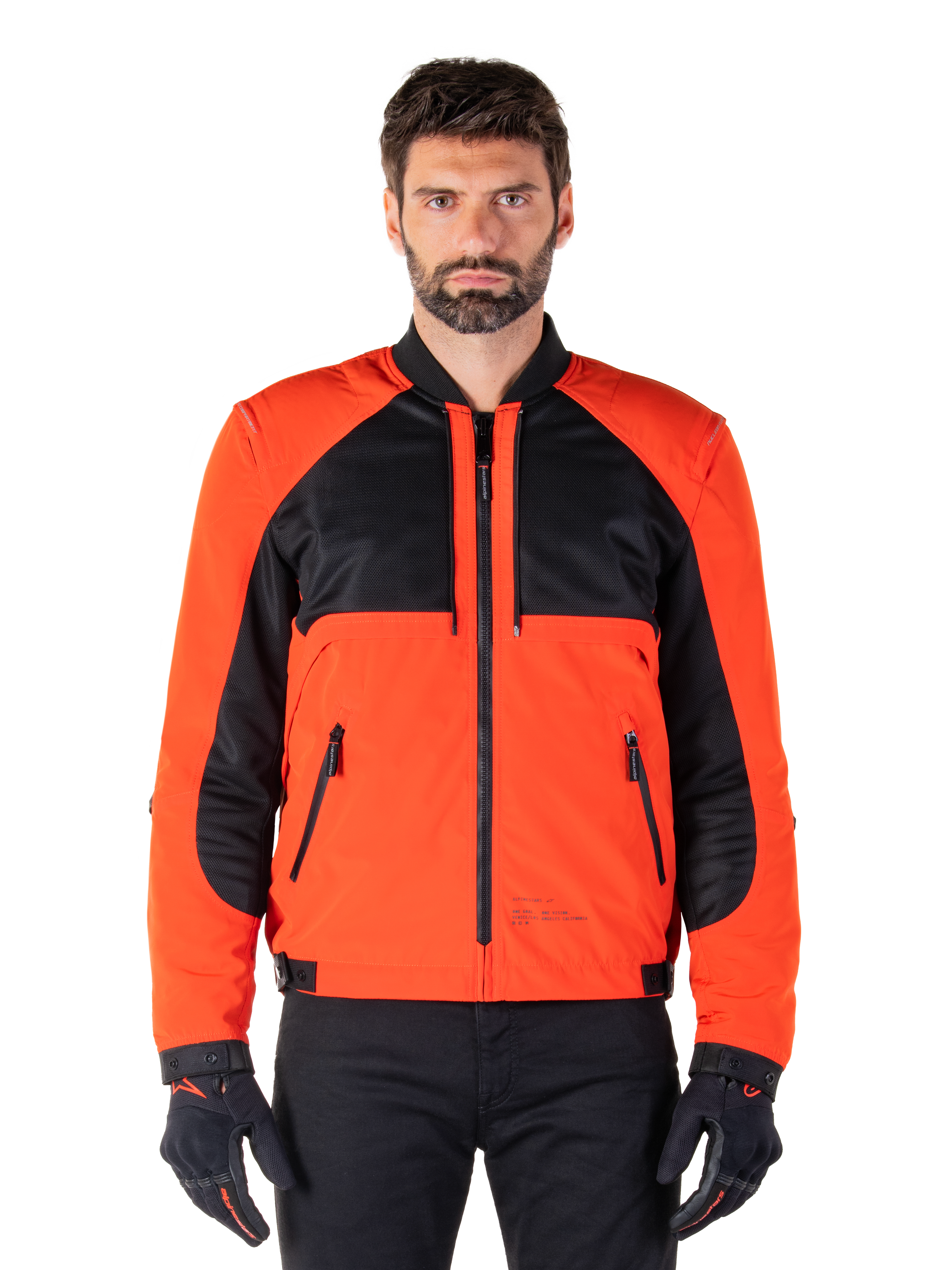 Alpinestars Mootant Wasserdichter Parka in Spicy Orange und Schwarz, modulare Motorradjacke in Bomberjacken-Konfiguration an einem männlichen Modell, mit schwarzen Mesh-Einsätzen im oberen Brustbereich, leuchtend orangefarbenem Torso und Ärmeln, Frontreißverschluss und Rippkragen, kombiniert mit schwarzen Handschuhen und einer schwarzen Hose.