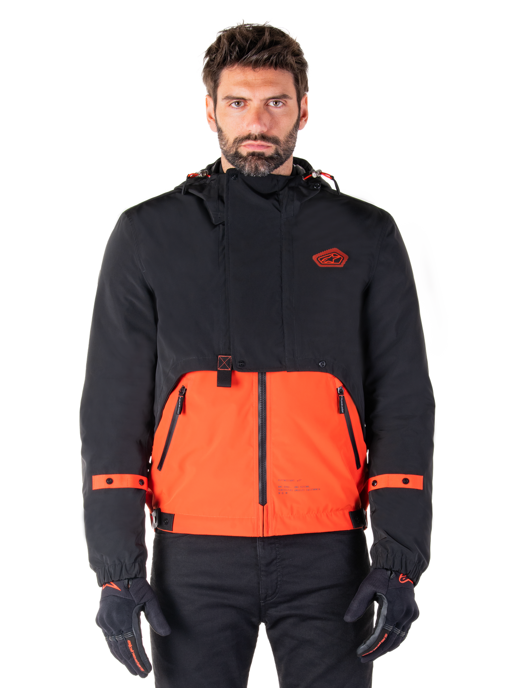 Alpinestars Mootant Waterproof Parka, modulare Motorradjacke in Spicy Orange und Schwarz, von einem Model mit passenden Handschuhen getragen, Kapuzendesign mit zweifarbigen Einsätzen, Frontreißverschluss und verstellbare Bündchen, moderne urbane Motorradbekleidung
