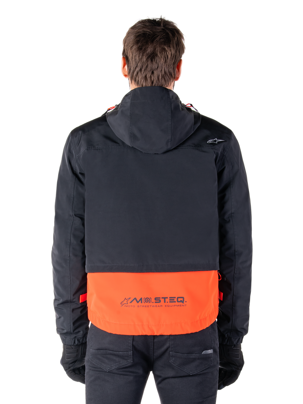 Alpinestars Mootant Waterproof Parka in Spicy Orange und Schwarz, Rückansicht mit schwarzem Oberteil und Kapuze, orangefarbener unterer Einsatz mit MO.ST.EQ. Wortmarke, funktionale Motorrad-Streetwear.
