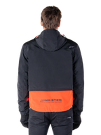 Alpinestars Mootant Waterproof Parka in Spicy Orange und Schwarz, Rückansicht mit schwarzem Oberteil und Kapuze, orangefarbener unterer Einsatz mit MO.ST.EQ. Wortmarke, funktionale Motorrad-Streetwear.