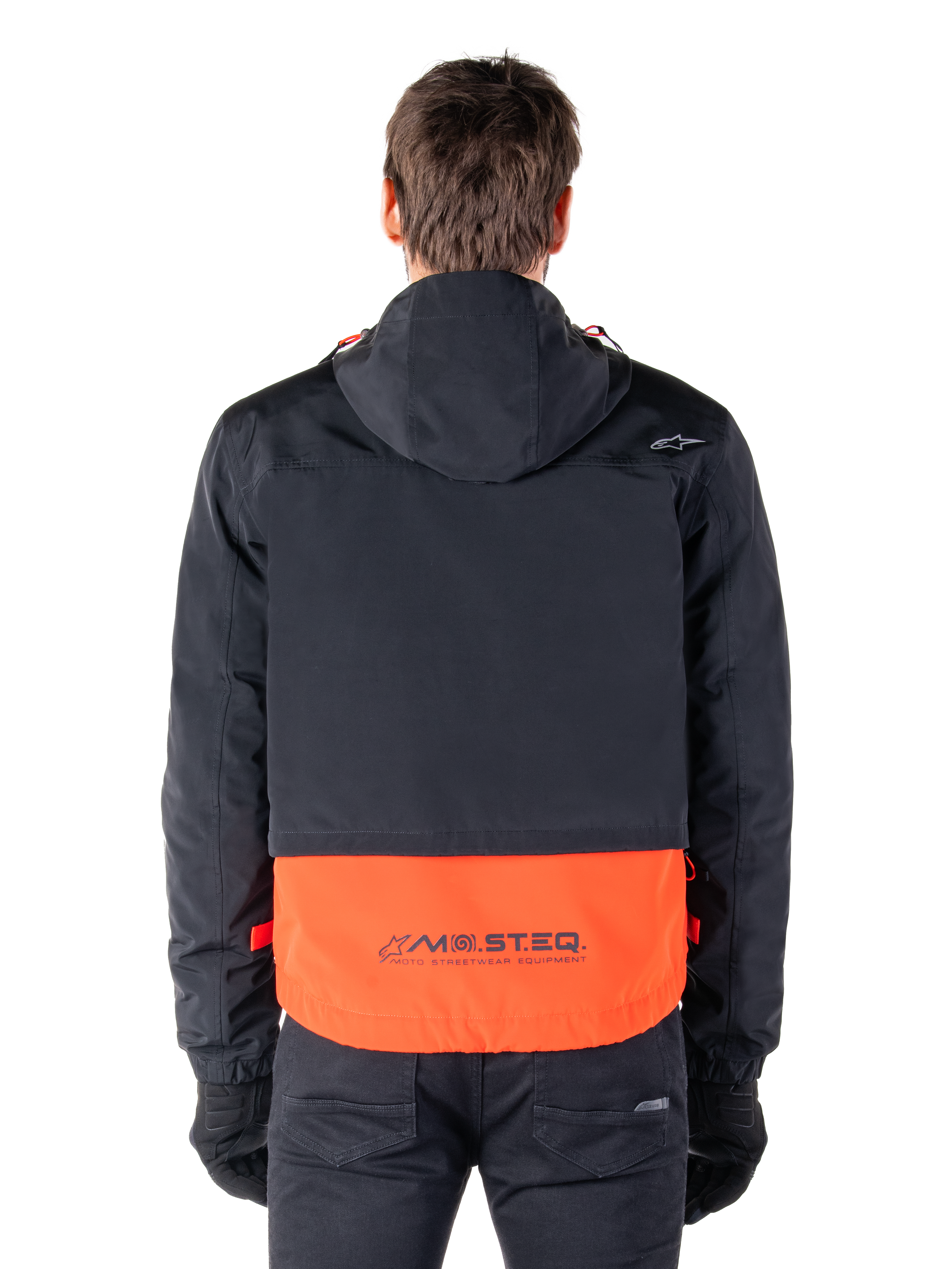 Alpinestars Mootant Waterproof Parka in Spicy Orange und Schwarz, Rückansicht mit schwarzem Oberteil und Kapuze, orangefarbener unterer Einsatz mit MO.ST.EQ. Wortmarke, funktionale Motorrad-Streetwear.