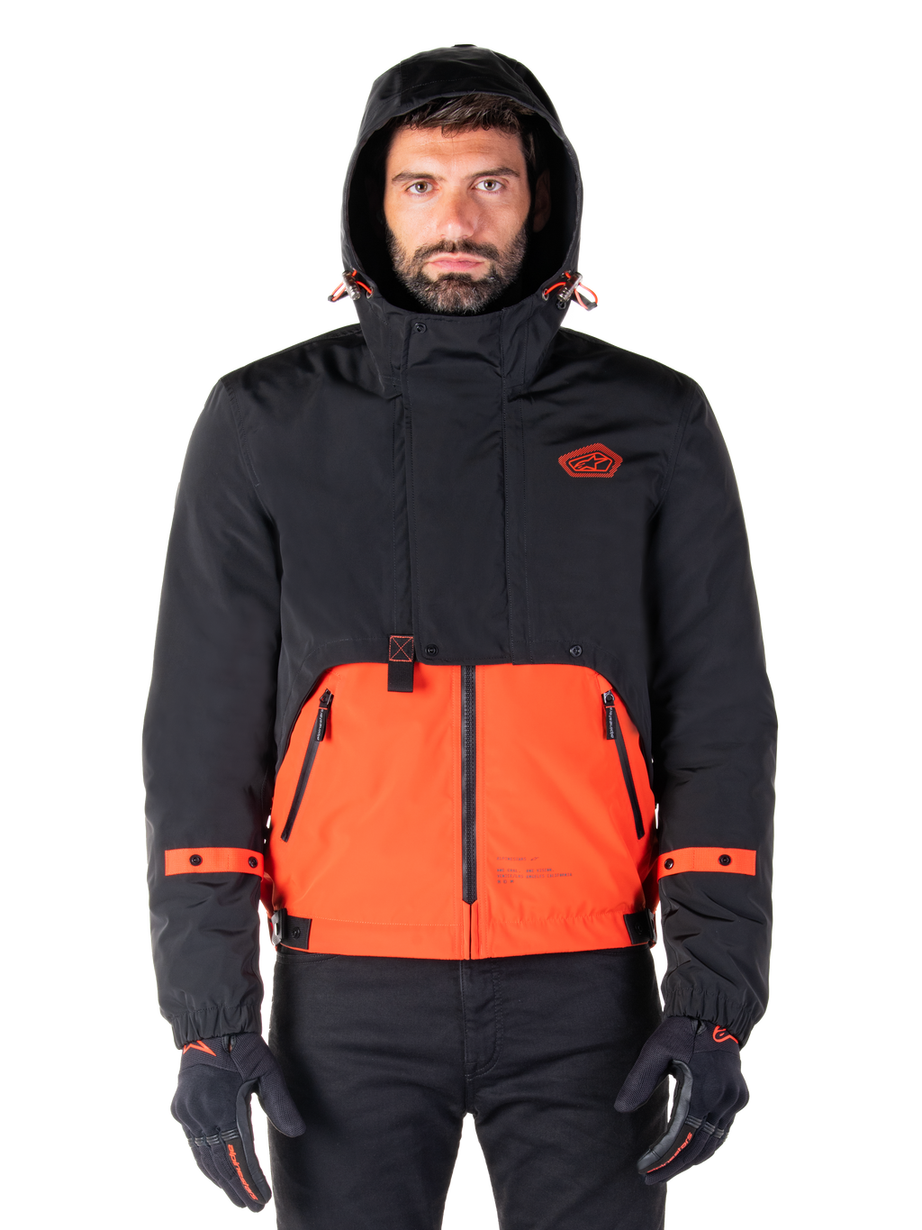 Alpinestars Mootant wasserdichter Parka, Motorradjacke, Spicy Orange und Schwarz, modulares Allwetter-Design mit Kapuze, Reißverschlusstaschen vorne und orangefarbene Riemendetails an den Ärmeln, getragen von einem Model mit schwarzen Handschuhen und Hosen