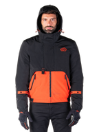 Alpinestars Mootant wasserdichter Parka, Motorradjacke, Spicy Orange und Schwarz, modulares Allwetter-Design mit Kapuze, Reißverschlusstaschen vorne und orangefarbene Riemendetails an den Ärmeln, getragen von einem Model mit schwarzen Handschuhen und Hosen