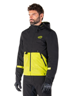 Alpinestars Mootant Waterproof Parka in Lime Punch Black, modular motorcycle jacket worn by a man with black riding gloves and pants, featuring a black upper section and sleeves with a vibrant lime green lower panel, hooded design with a utilitarian military-inspired aesthetic.