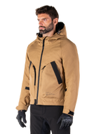 Alpinestars Morush Wasserdichter Parka, Utility Brown, männliches Model trägt Parka mit schwarzen Motorradhandschuhen und schwarzer Hose, minimalistisches, von Streetwear inspiriertes Design mit sturmsicherer Kapuze und großen Vordertaschen, wasserdichte Motorradbekleidung