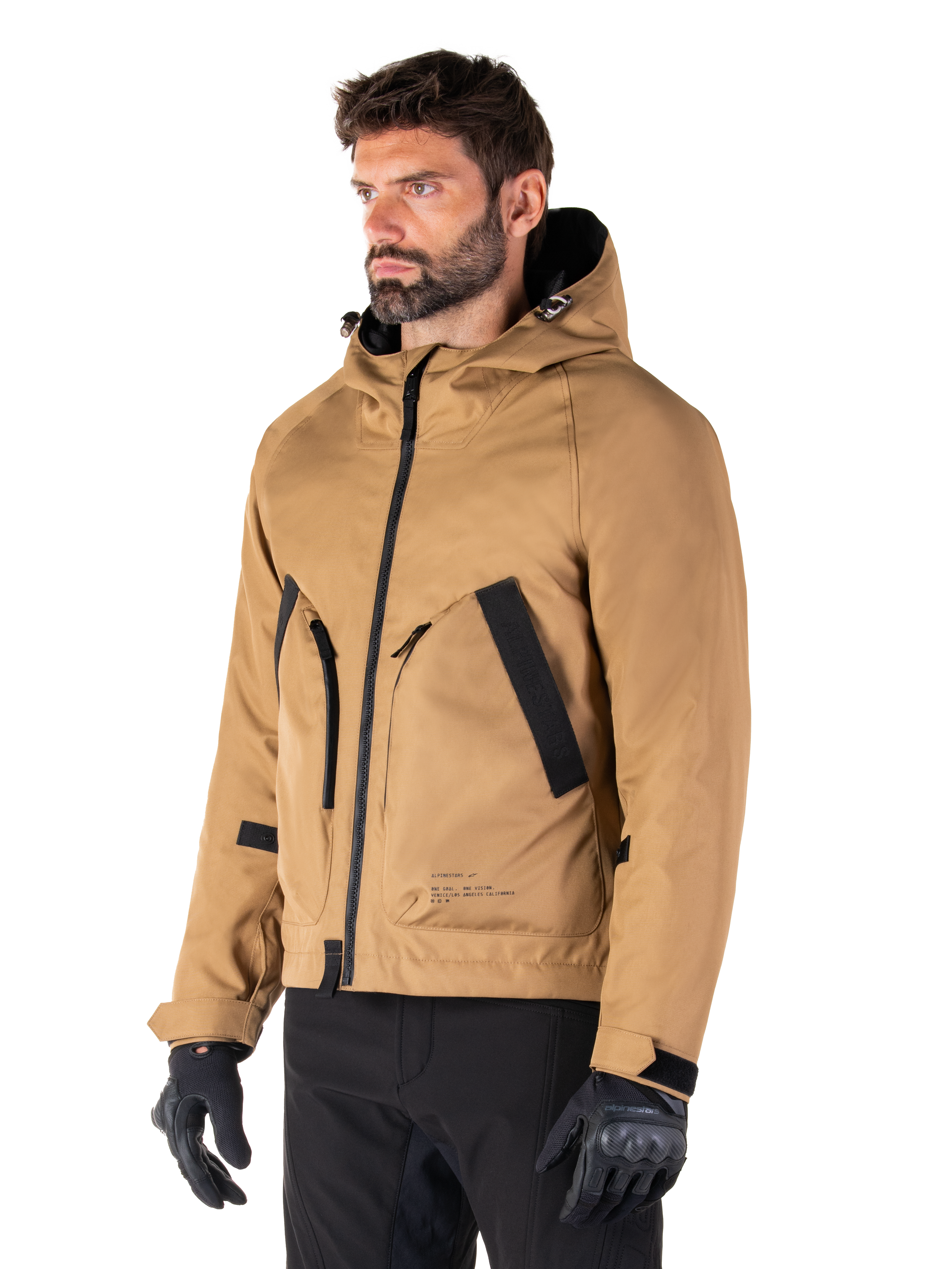 Alpinestars Morush Wasserdichter Parka, Utility Brown, männliches Model trägt Parka mit schwarzen Motorradhandschuhen und schwarzer Hose, minimalistisches, von Streetwear inspiriertes Design mit sturmsicherer Kapuze und großen Vordertaschen, wasserdichte Motorradbekleidung