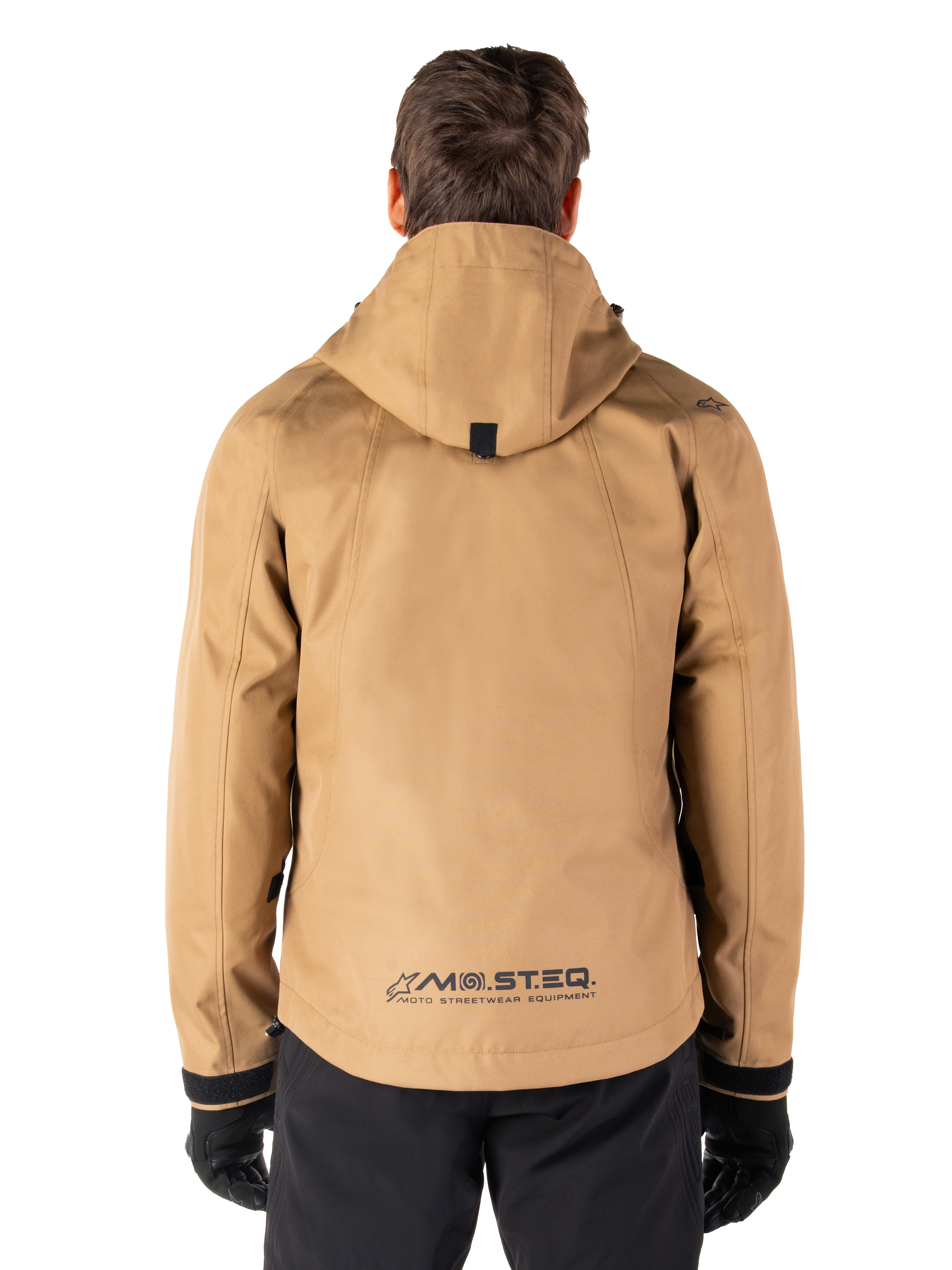 Alpinestars Morush Wasserdichter Parka, Utility Brown, Rückansicht, mit Kapuze und MO.ST.EQ.-Branding am unteren Rücken, kombiniert mit schwarzer Hose und Handschuhen, moderne von Streetwear inspirierte Motorradbekleidung