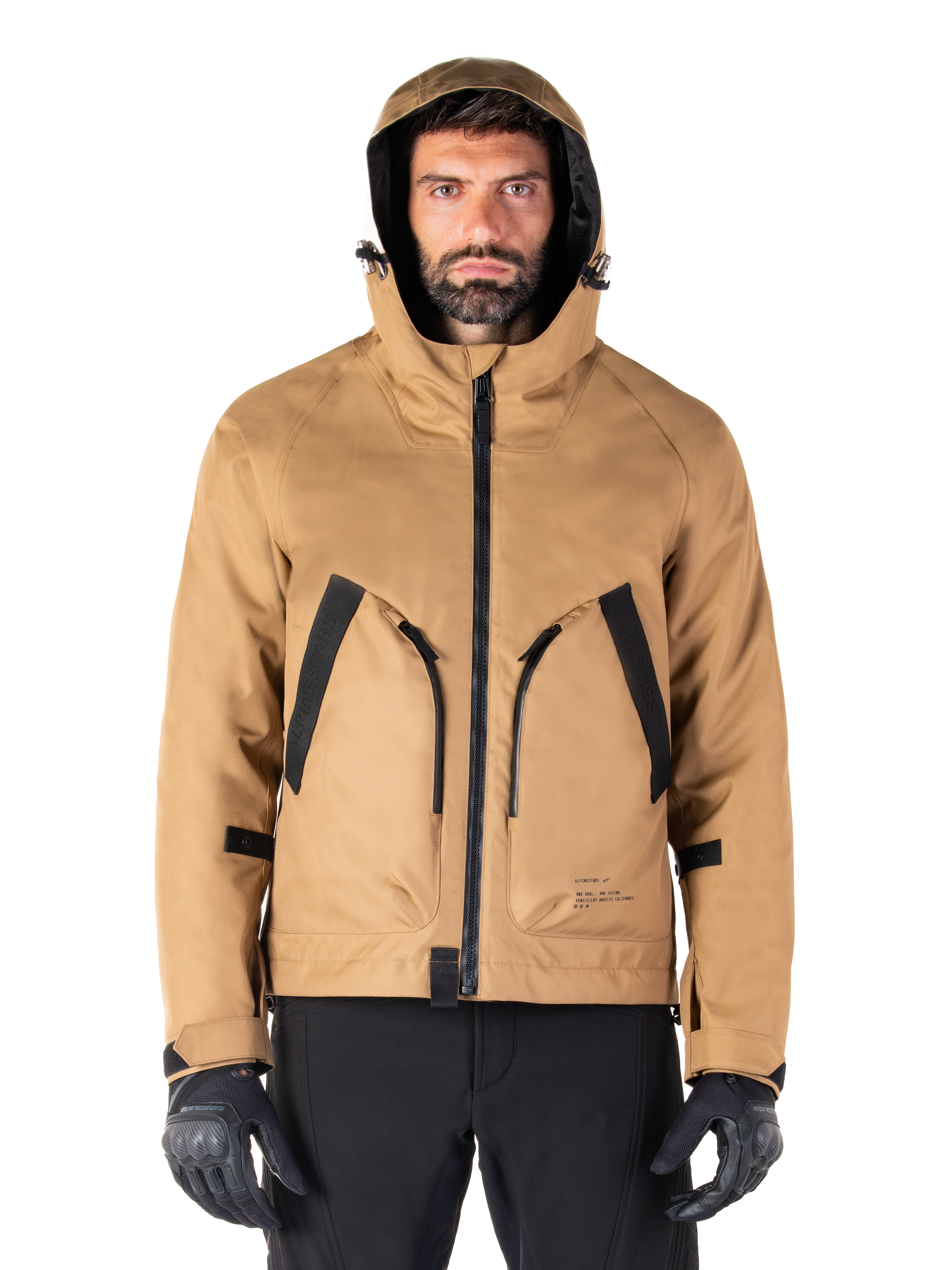 Alpinestars Morush Wasserdichter Parka, Motorradjacke, Utility Brown, Kapuzendesign im Streetwear-Stil mit großen, schwarz akzentuierten Fronttaschen, kombiniert mit schwarzen Fahrhandschuhen und Hosen, moderne urbane Motorradausrüstung