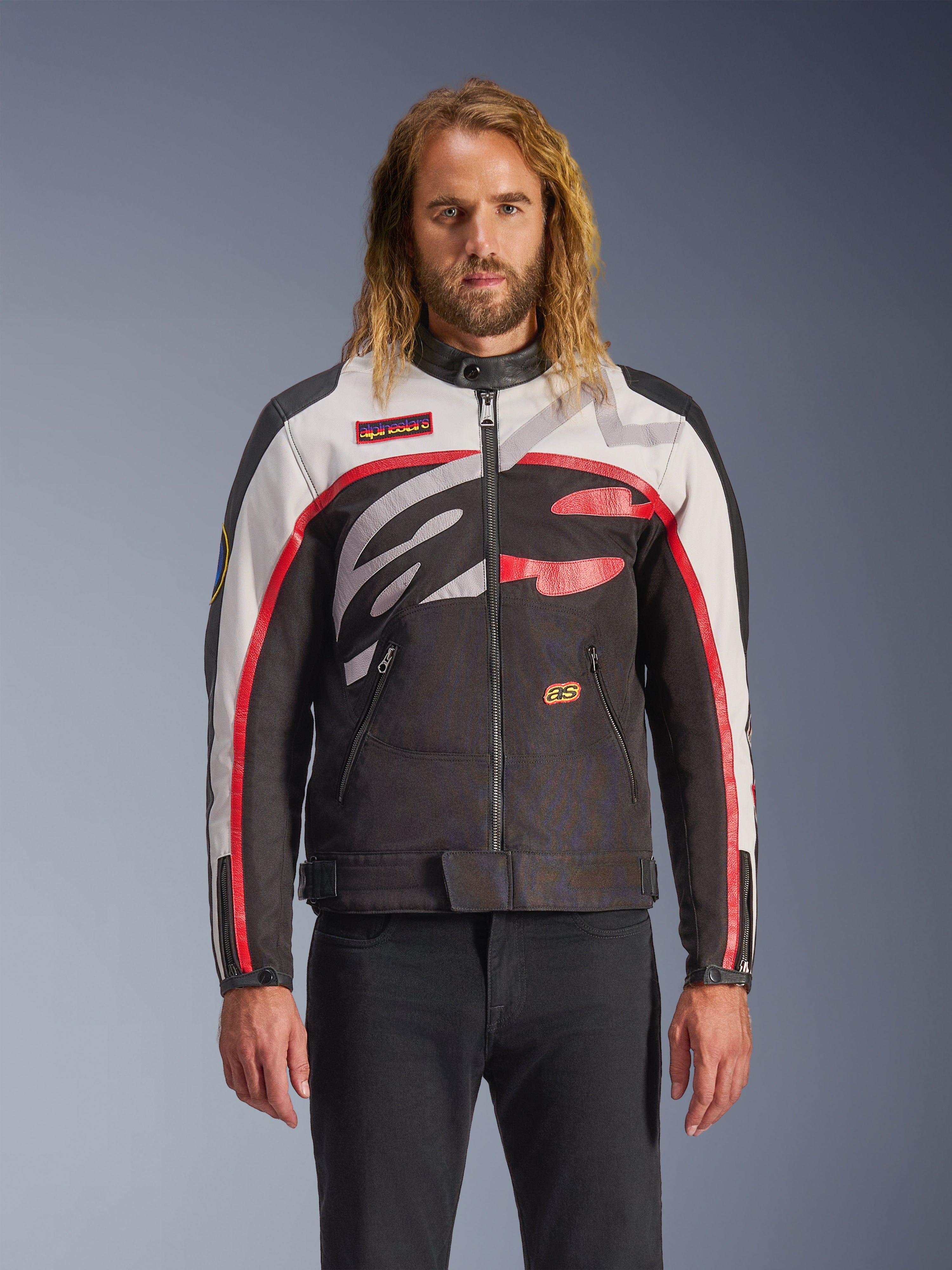 Alpinestars Axton Jacket, Motorcycle Jacket, Black Off White and Bright Red, featuring bold abstract chest patterns and wrap-around logo, red striped sleeves, vintage-inspired design with a minimalist collar, worn by model with black jeans.