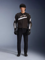 Alpinestars T-GP Plus R V4 Jacke, Schwarz und Weiß, Sport-Textilmotorradjacke, getragen von einem Modell mit schwarzer Hose und Handschuhen, mit markantem weißen Alpinestars-Logo auf der Brust und den Ärmeln, schlankes, vom Rennsport inspiriertes Design