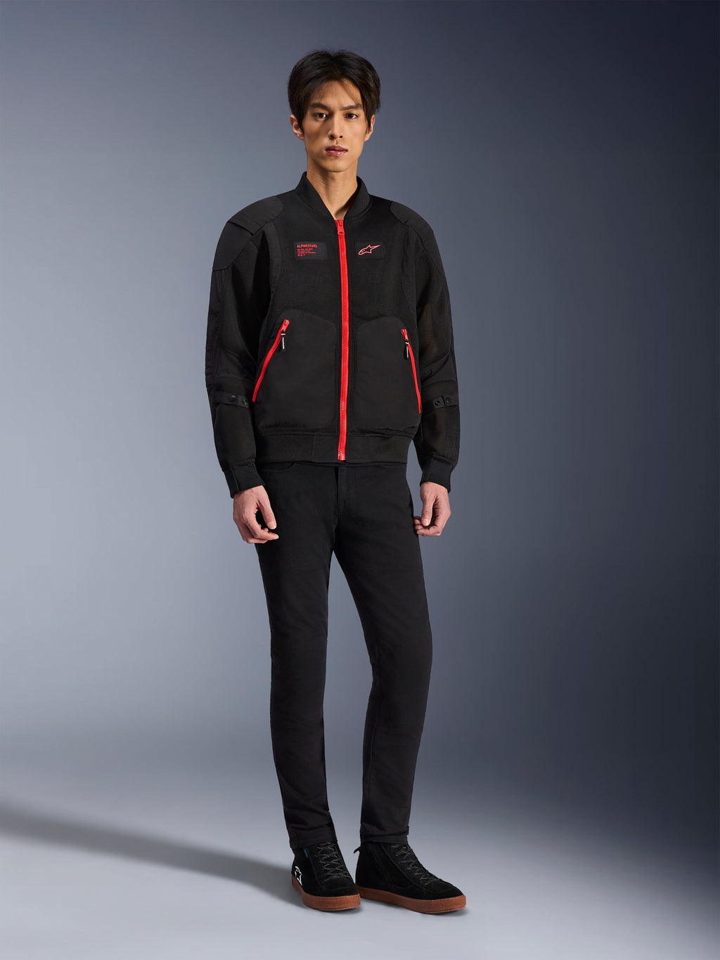 Alpinestars Flight Air Jacke in Black Bright Red, urbane Motorradjacke im Bomber-Stil mit 3D-Mesh-Einsätzen und leuchtend roten Reißverschlüssen, getragen von einem Modell mit schwarzer Slim-Fit-Hose und schwarzen Sneakern, Streetwear-inspirierte moderne Fahrausrüstung