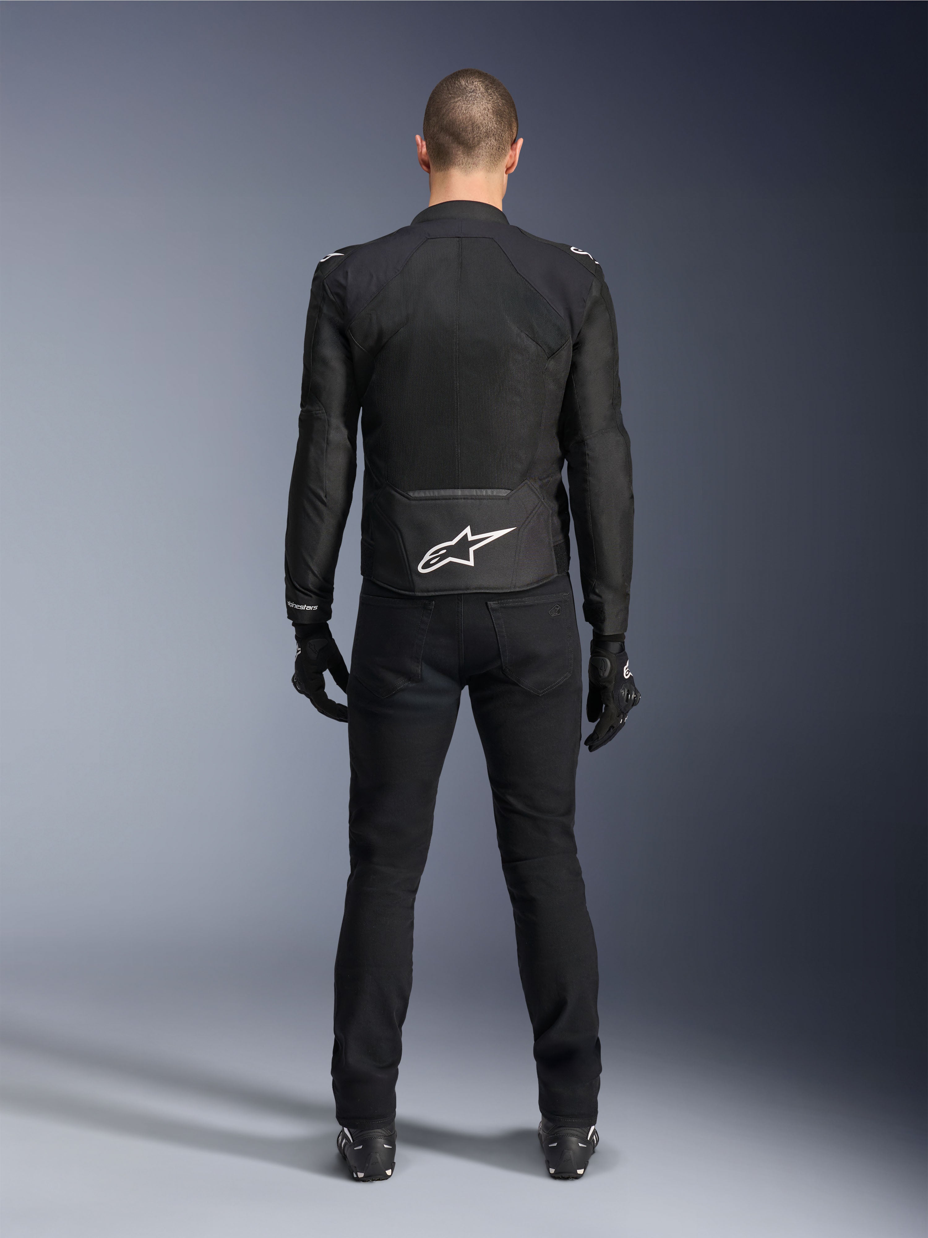 Alpinestars Viper Air V4 Jacke, schwarze Textil-Motorradjacke, Rückansicht mit weißem Alpinestars Stern-Logo auf dem unteren Rücken, kombiniert mit schwarzer Motorradhose und Handschuhen, Sommerausrüstung für Straßen- und Sportfahrten