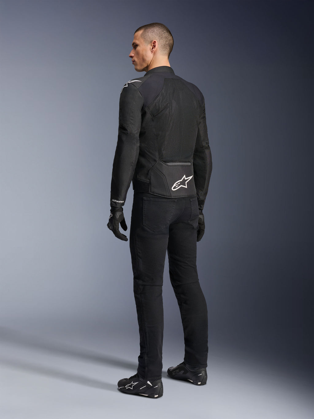 Alpinestars Viper Air V4 Jacke, schwarze Textil-Motorradjacke, Rückansicht an einem männlichen Model, mit großen Tech-Mesh-Einsätzen für Luftzirkulation und weißem Stern-Logo auf dem unteren Rücken, getragen mit passender schwarzer Motorradhose und Handschuhen