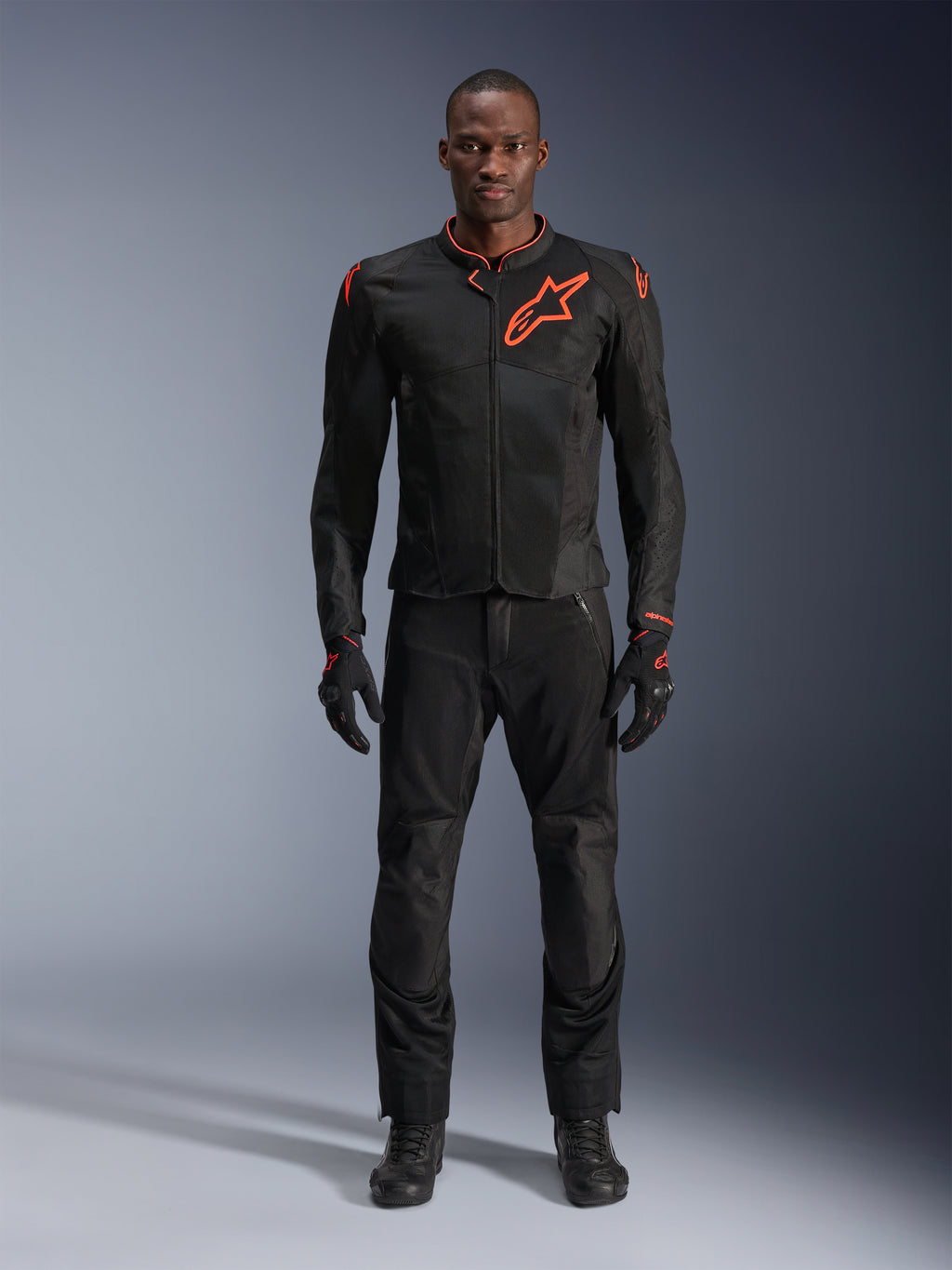 Alpinestars Viper Air V4 Jacke in Schwarz Rot Fluo, getragen von einem Modell mit passender schwarzer Hose und Handschuhen, mit Mesh-Einsätzen für Luftzirkulation und einem markanten roten Alpinestars-Logo auf der Brust, sportliche Motorrad-Straßenausrüstung.