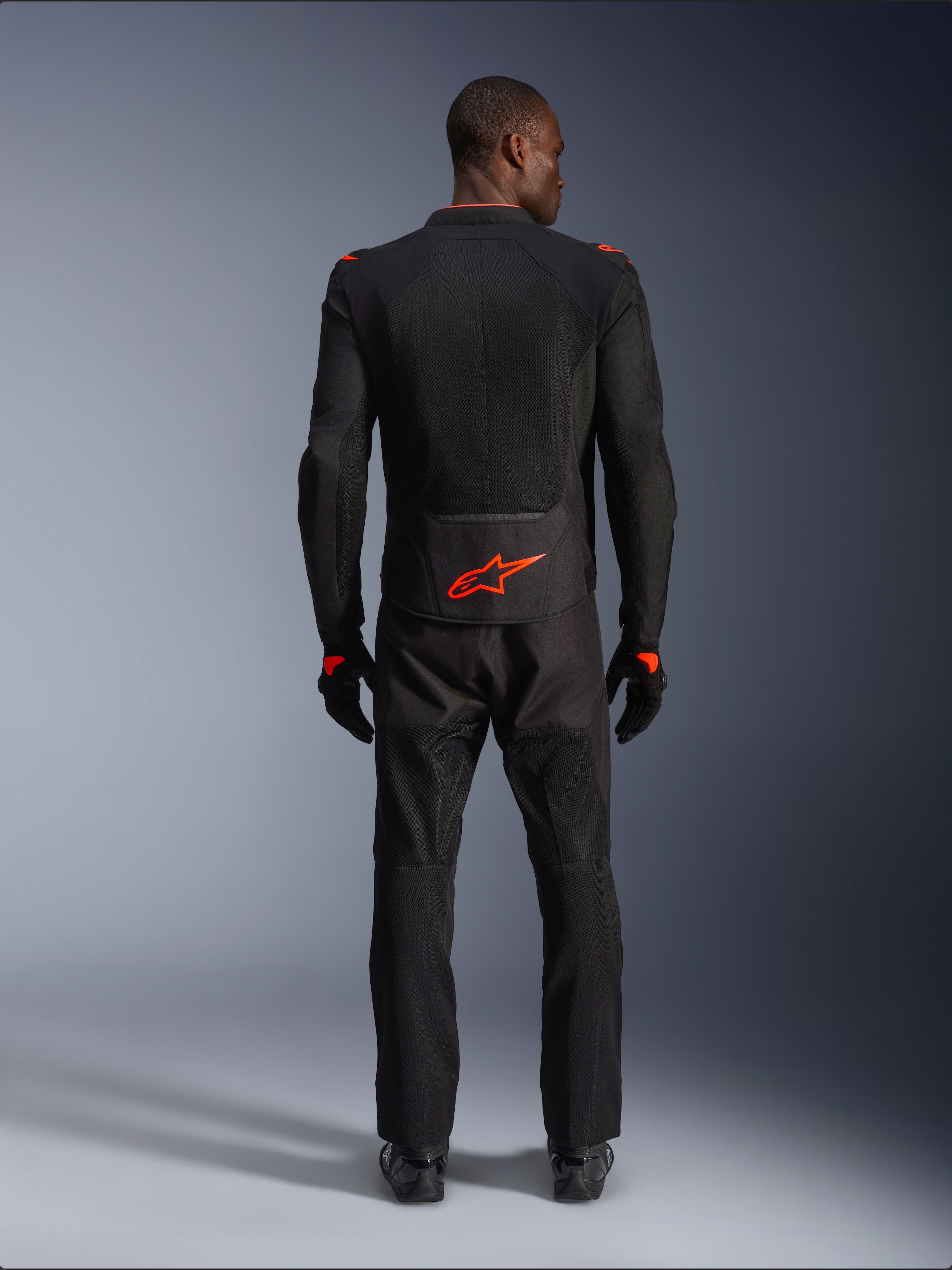 Alpinestars Viper Air V4 Jacke, Schwarz und Rot Fluo, Rückansicht am Modell, getragen mit passender schwarzer Motorradhose und Handschuhen, mit einem leuchtend fluoreszierenden roten Logo auf dem unteren Rücken, Mesh-Konstruktion für optimale Luftzirkulation, sportliche Passform für das Motorradfahren auf der Straße