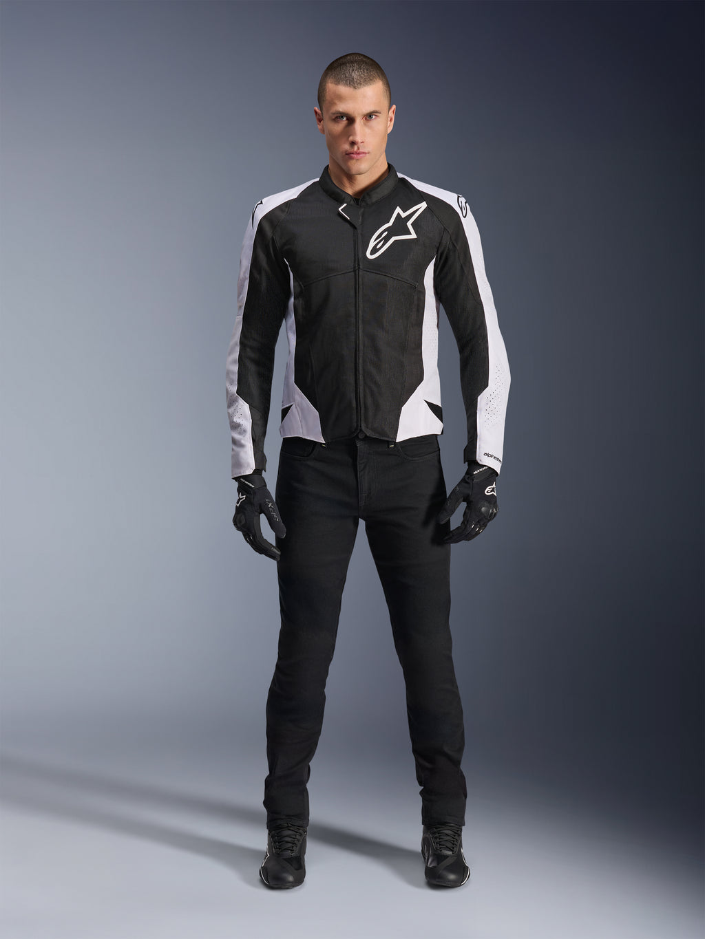Alpinestars Viper Air V4 Jacke, schwarz-weiße Motorradjacke mit großem weißem Logo auf der Brust, getragen von einem männlichen Model mit schwarzer Hose und Handschuhen, mit Mesh-Panels zur Belüftung, sportliche Straßenmotorradbekleidung