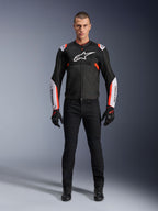 Männliches Model in der Alpinestars T-Sps Air V2 Jacke in Schwarz Weiß Rot Fluo, mit großen Tech-Mesh-Einsätzen und markantem weißem Branding auf Brust und Ärmeln, kombiniert mit schwarzer technischer Motorradhose und Handschuhen, urbane Sport-Motorradausrüstung