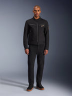 Alpinestars Bruiser Jacke, schwarze urbane Motorradjacke, getragen von einem Model mit schwarzer Hose und High-Top-Sneakern, Vorderansicht mit Brusttaschen mit Reißverschluss und besticktem Logo, klassisches, von Workwear inspiriertes Design für den täglichen Weg zur Arbeit