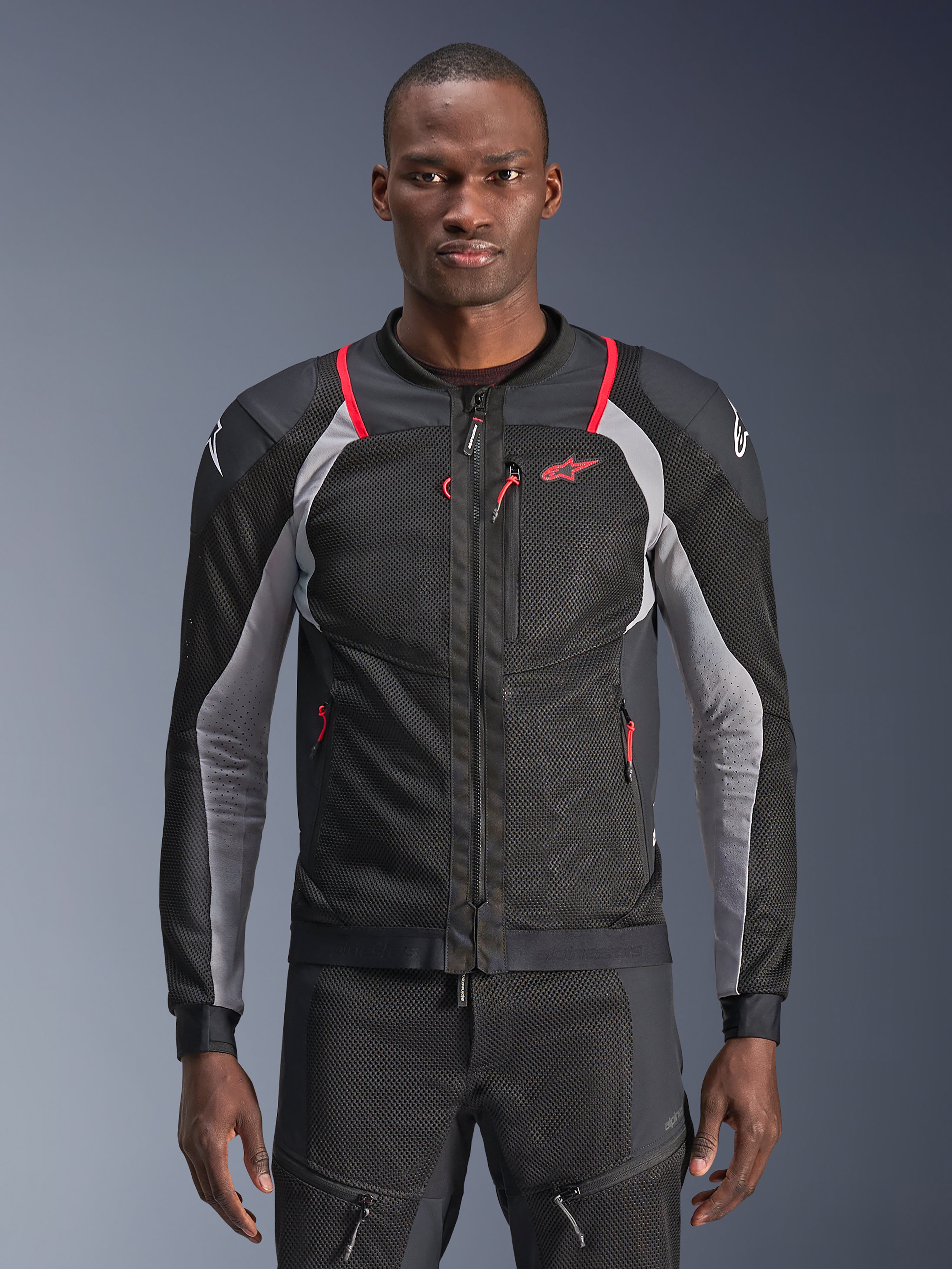 Alpinestars Troop-Air Pro Jacke, Schwarz, Ash Gray und Bright Red, von einem Model getragen, Motorrad-Mesh-Jacke mit perforierten Belüftungspaneelen, roten Reißverschlusstaschen und weißen Schulterlogos, technische gepanzerte Fahrausrüstung