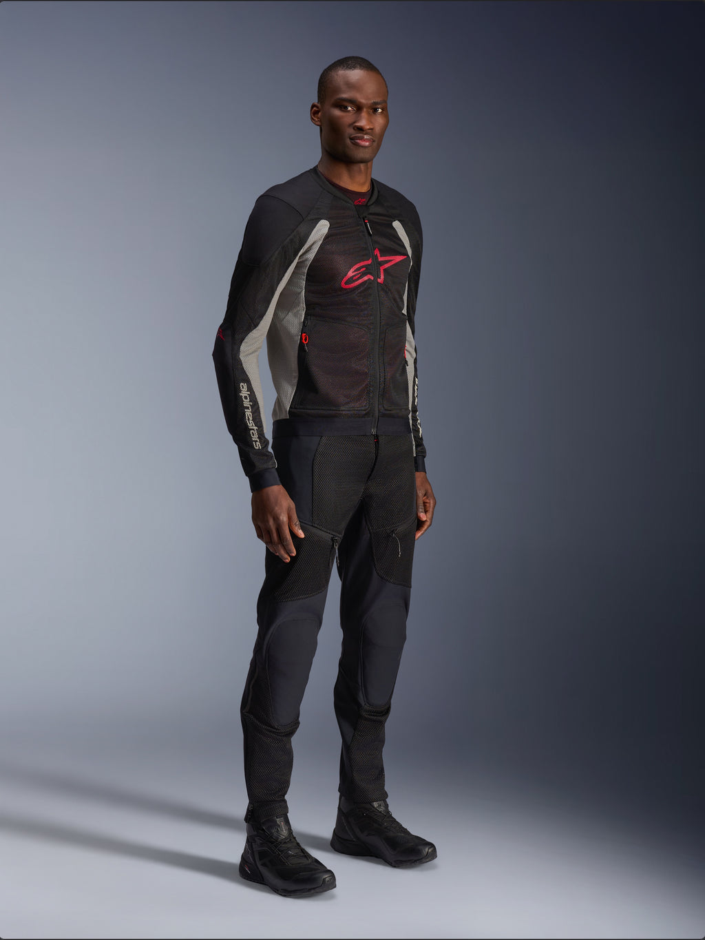 Alpinestars Troop-Air Jacket, technical mesh motorcycle jacket in Black, Ash Gray and Bright Red, worn by a model with matching black pants and boots, featuring a red Alpinestars logo on the chest, urban contemporary riding gear.