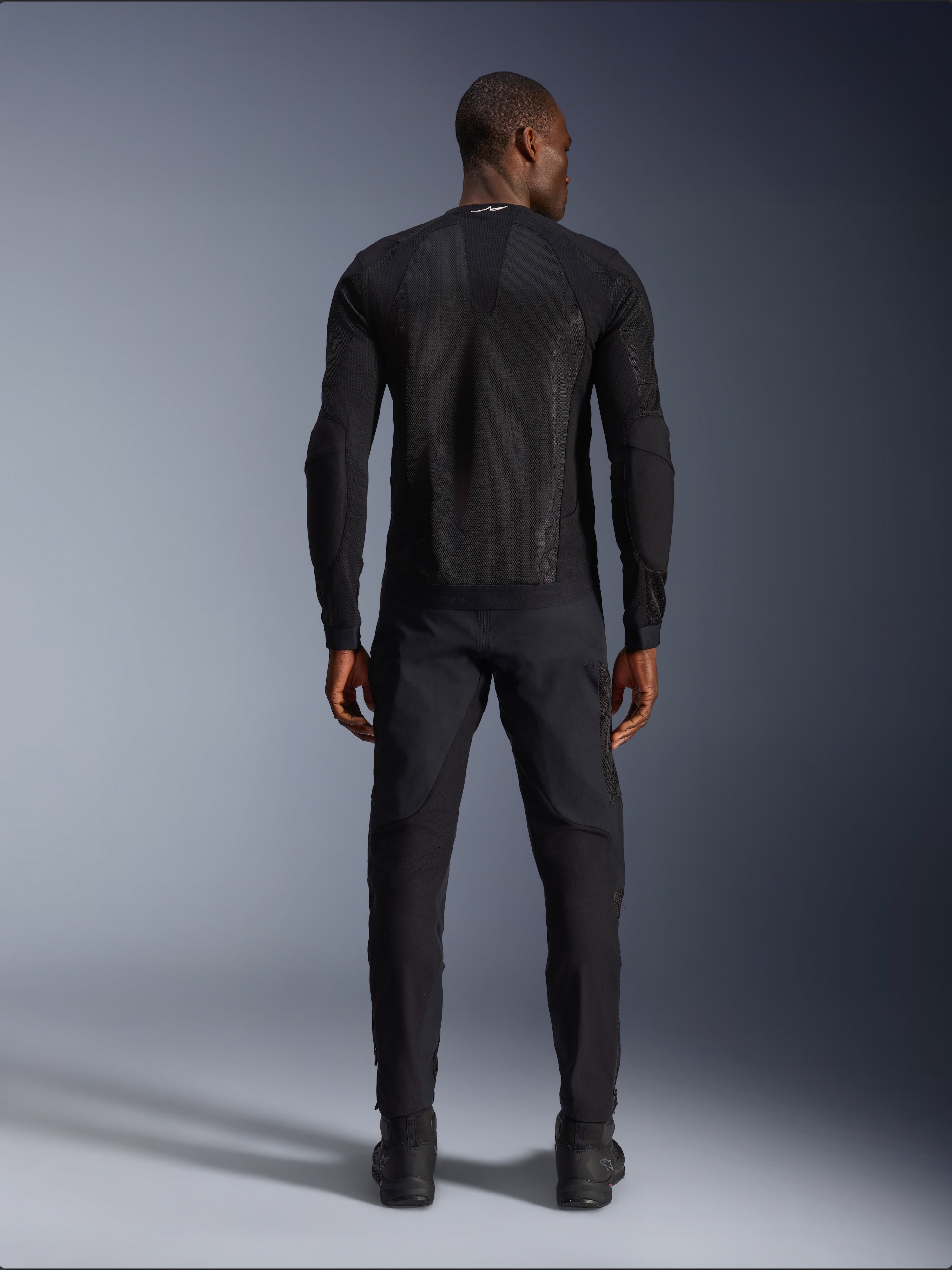 Alpinestars Troop-Air Jacke in Schwarz, Rückansicht mit technischem Mesh-Rückeneinsatz und belüfteter Konstruktion, kombiniert mit passender schwarzer Motorradhose und Stiefeln.