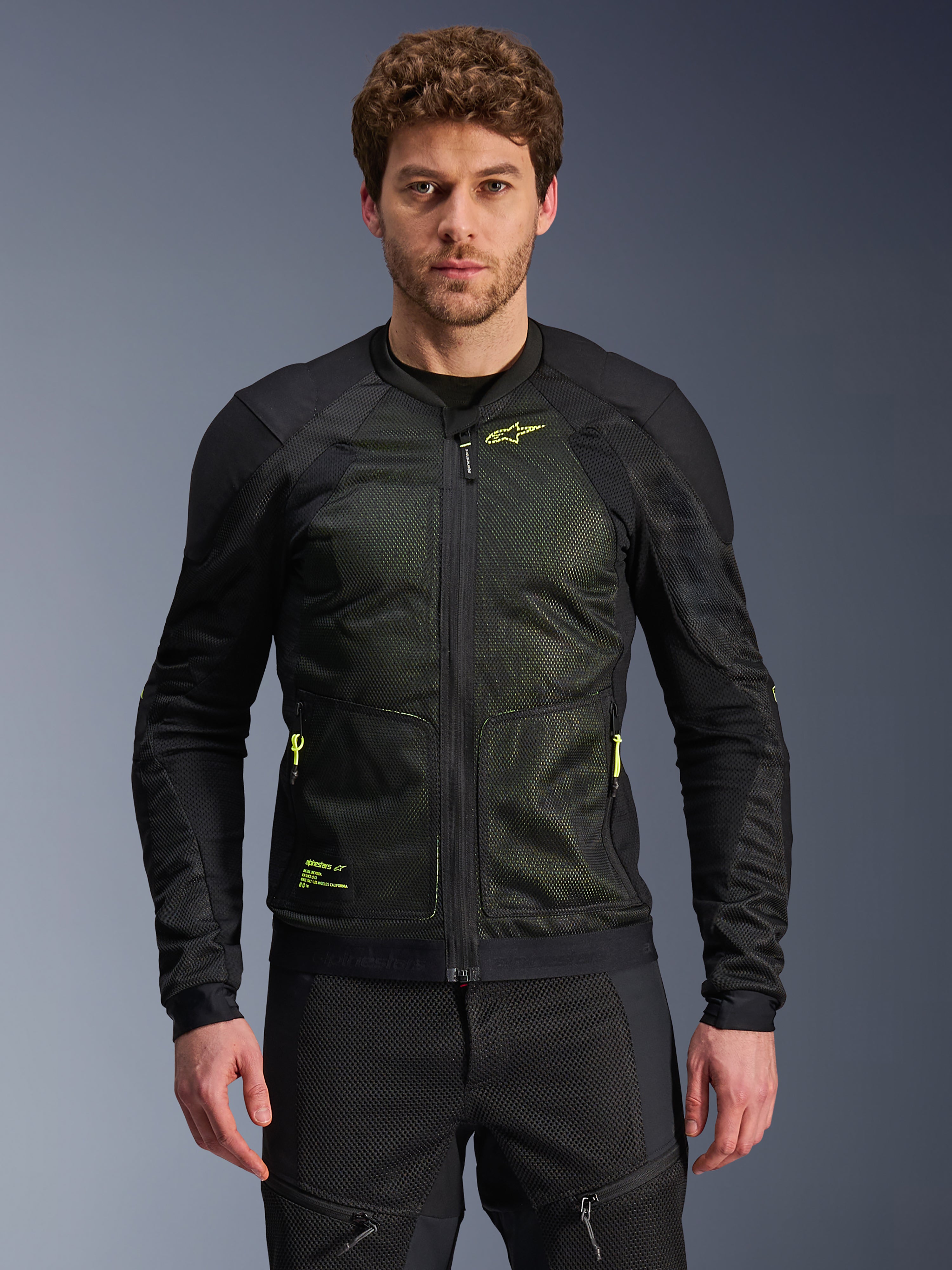 Alpinestars Troop-Air Jacke, Schwarz und Gelb Fluo, getragen von einem männlichen Model, mit leichter Mesh-Konstruktion, neongelben Reißverschlüssen und Branding, technische belüftete Motorradjacke für urbanes Fahren