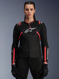 Alpinestars Stella T-Sps Air V2 Damenjacke, Schwarz und Diva Pink, Textil-Motorradjacke mit atmungsaktiven Mesh-Einsätzen und pinkfarbenen Akzenten, weißes Alpinestars-Logo auf der Brust, getragen von einem weiblichen Model mit schwarzer Fahrhose und Handschuhen.