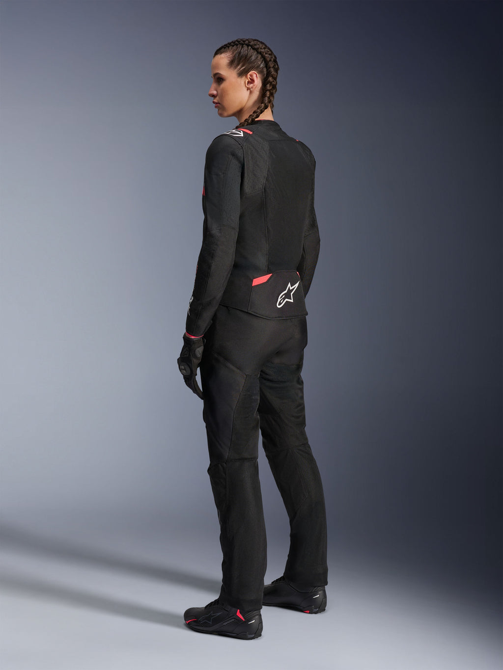 Alpinestars Stella T-Sps Air v2 Damenjacke, Schwarz und Diva Pink, Textil-Motorradjacke in der Rückansicht mit großen Mesh-Einsätzen für Luftzirkulation und weißem Stern-Logo auf dem Rücken, getragen mit passender schwarzer Fahrhose, Handschuhen und Stiefeln.