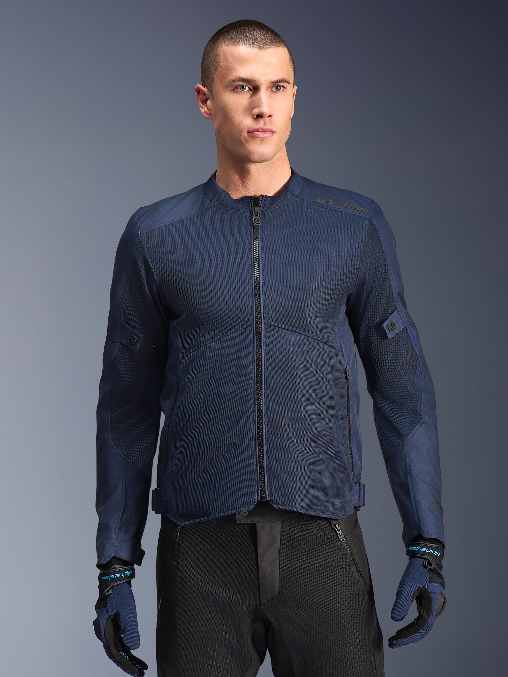 Alpinestars C-1 Air Jacke, blaue Motorradjacke, getragen von einem männlichen Model mit schwarzer Hose und passenden blau-schwarzen Handschuhen, Tech-Mesh-Einsätze für optimalen Luftstrom, cleanes urbanes Design mit Frontreißverschluss und dezentem Branding
