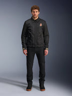 Männliches Model in der Alpinestars Ignite Air Jacke in Schwarz, mit klassischem Hemdkragen, Frontreißverschluss und einem orangefarbenen Logo auf der Brust. Kombiniert mit einer schwarzen Hose und schwarzen High-Top-Sneakern für einen modernen, urbanen Motorrad-Look.