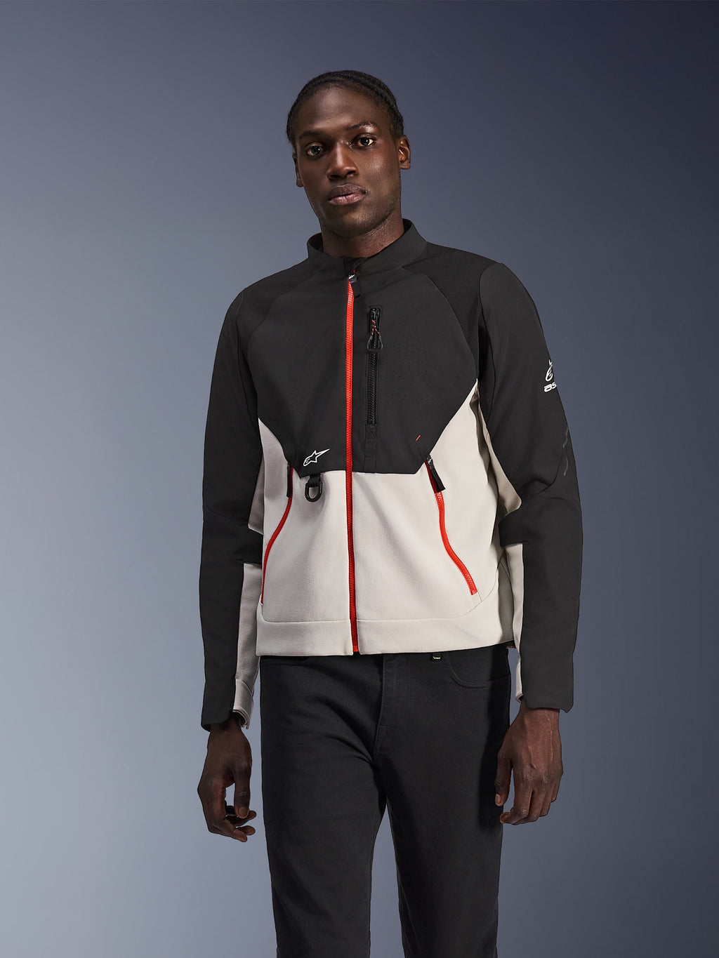 Alpinestars Provoke Jacke, urbane Motorradjacke, Schwarz und Hellgrau mit leuchtend roten Reißverschlüssen, hoher Kragen, mit Logo-Details auf der Brust und am Ärmel, modernes schützendes straßentaugliches Design, von einem Modell getragen