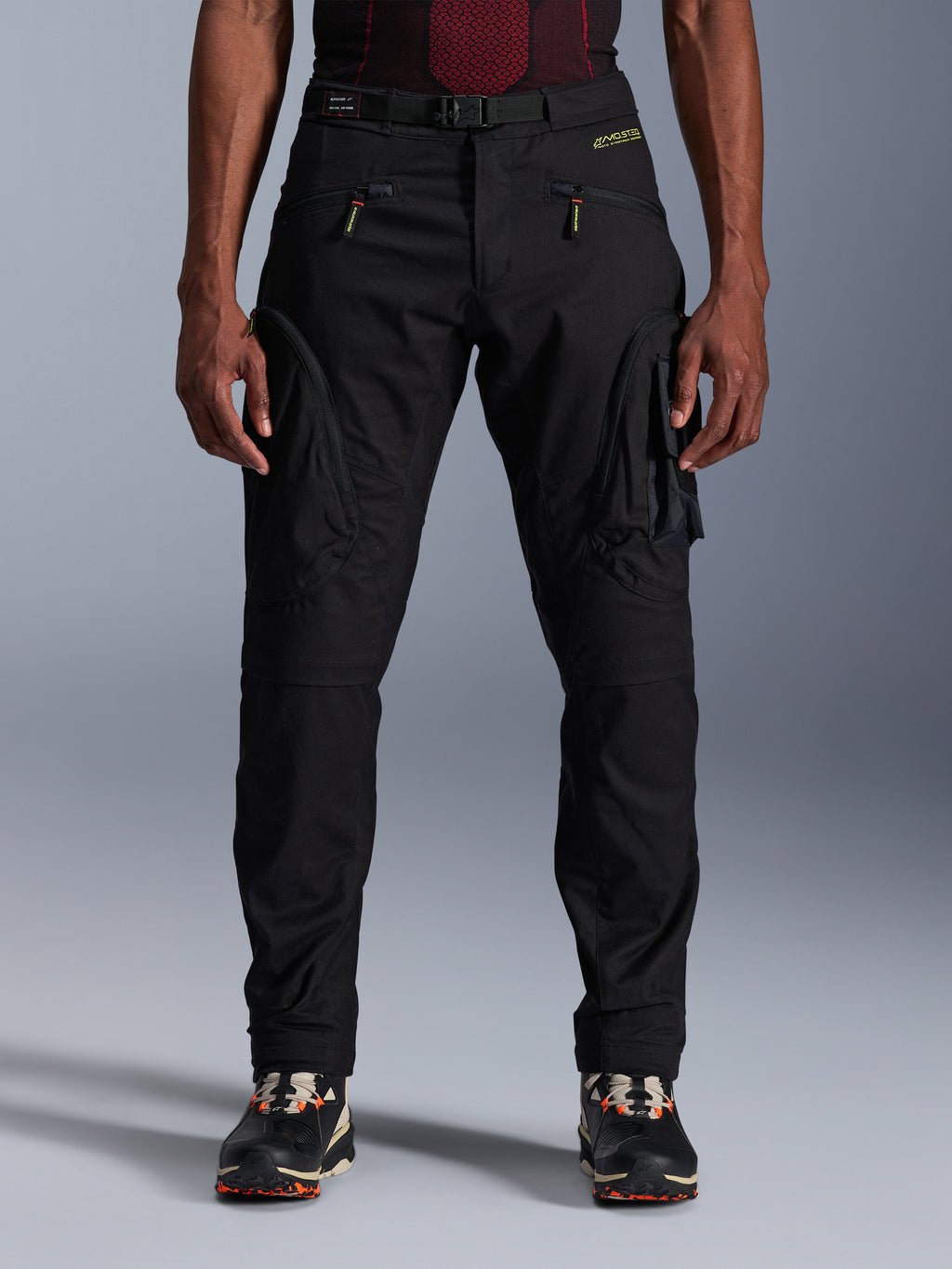 Alpinestars Acteon Hose, schwarze Urban-Motorradhose, Tapered Regular Fit, seitliche Cargotaschen mit umgekehrten Spiralreißverschlüssen, integrierter Gürtel und gelbes Branding, schützende Textil-Motorradausrüstung