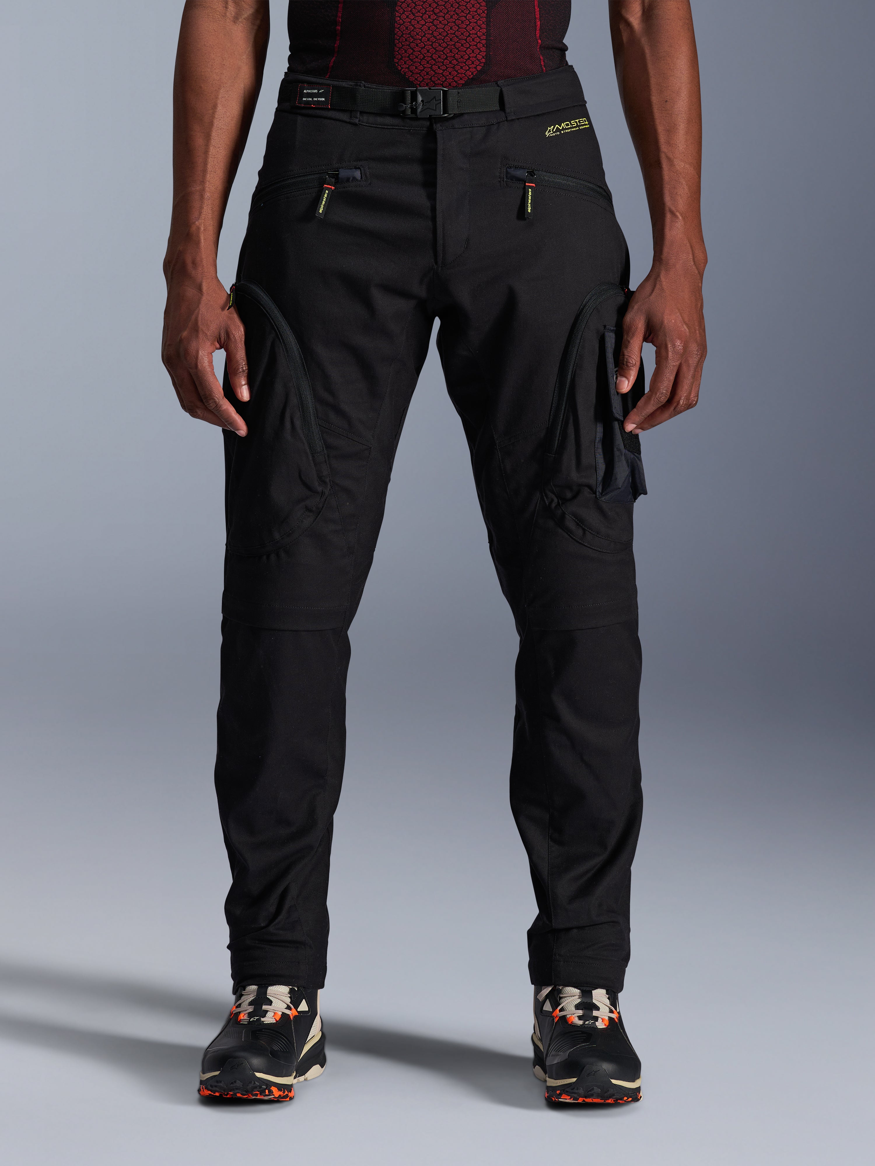 Alpinestars Acteon Hose, schwarze Urban-Motorradhose, Tapered Regular Fit, seitliche Cargotaschen mit umgekehrten Spiralreißverschlüssen, integrierter Gürtel und gelbes Branding, schützende Textil-Motorradausrüstung