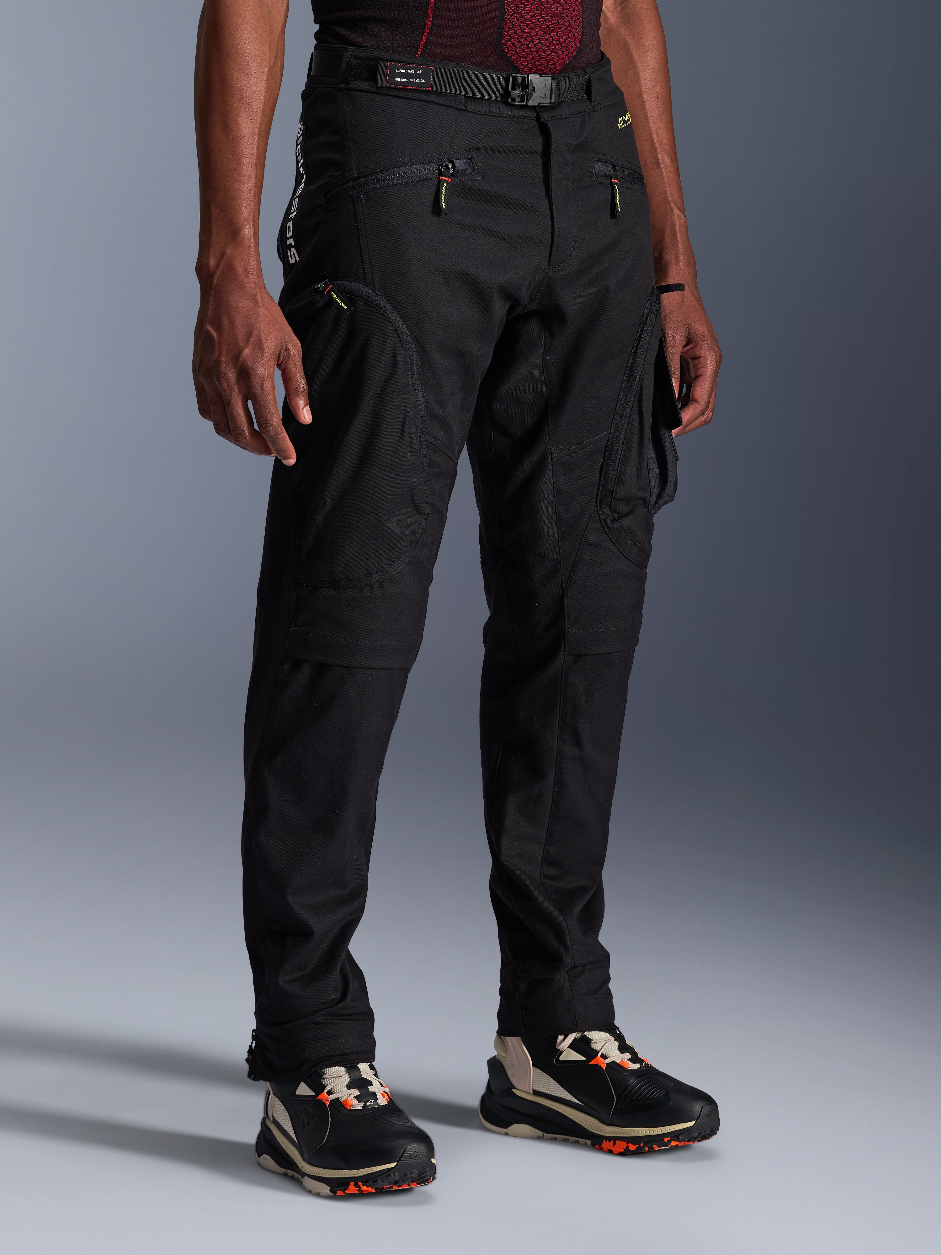 Alpinestars Acteon Hose, schwarze Motorradhose, an einem Model präsentiert, mit moderner, schmal zulaufender Silhouette, Cargo-Taschen mit Reißverschluss, verstellbarem Taillengürtel und technischen Sneakers, urbane Motorradbekleidung