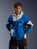Männliches Model trägt die Alpinestars Mogress Air Jacke in Blue Almond, urbane Motorradjacke mit Color-Blocking in leuchtendem Blau und Navy, cremefarbenen Akzenten an Kapuze und Taschen, technisches Ripstop-Gewebe mit Utility-Taschen, moderne vom Motorsport inspirierte Streetwear.