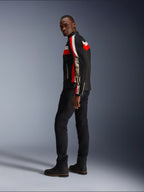 Ein Mann in der Alpinestars T-Dyno Air Jacke in Schwarz, Bright Red und Ecru, vintage-inspirierte Textil-Motorradjacke mit Mesh-Einsätzen, markantes Branding auf dem Ärmel, kombiniert mit schwarzer Hose und Stiefeln für einen modernen Biker-Look