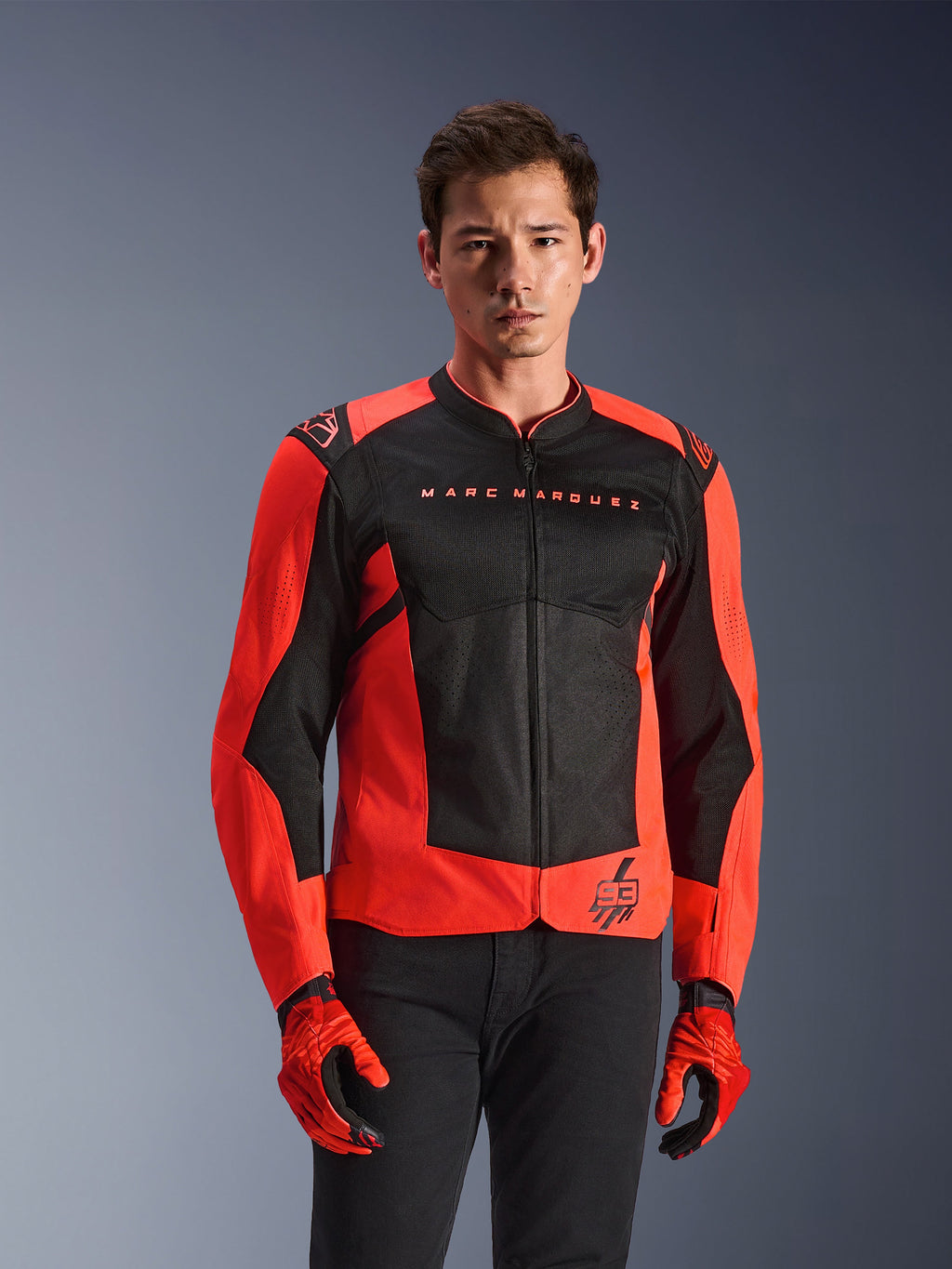Alpinestars MM93 T-SPS Air V2 Jacke, Motorradjacke, Rot Fluo und Schwarz, getragen von einem Modell mit passenden roten Handschuhen und schwarzer Hose, mit 'Marc Marquez'-Branding auf der Brust und '93'-Logo, sportliche Mesh-Konstruktion